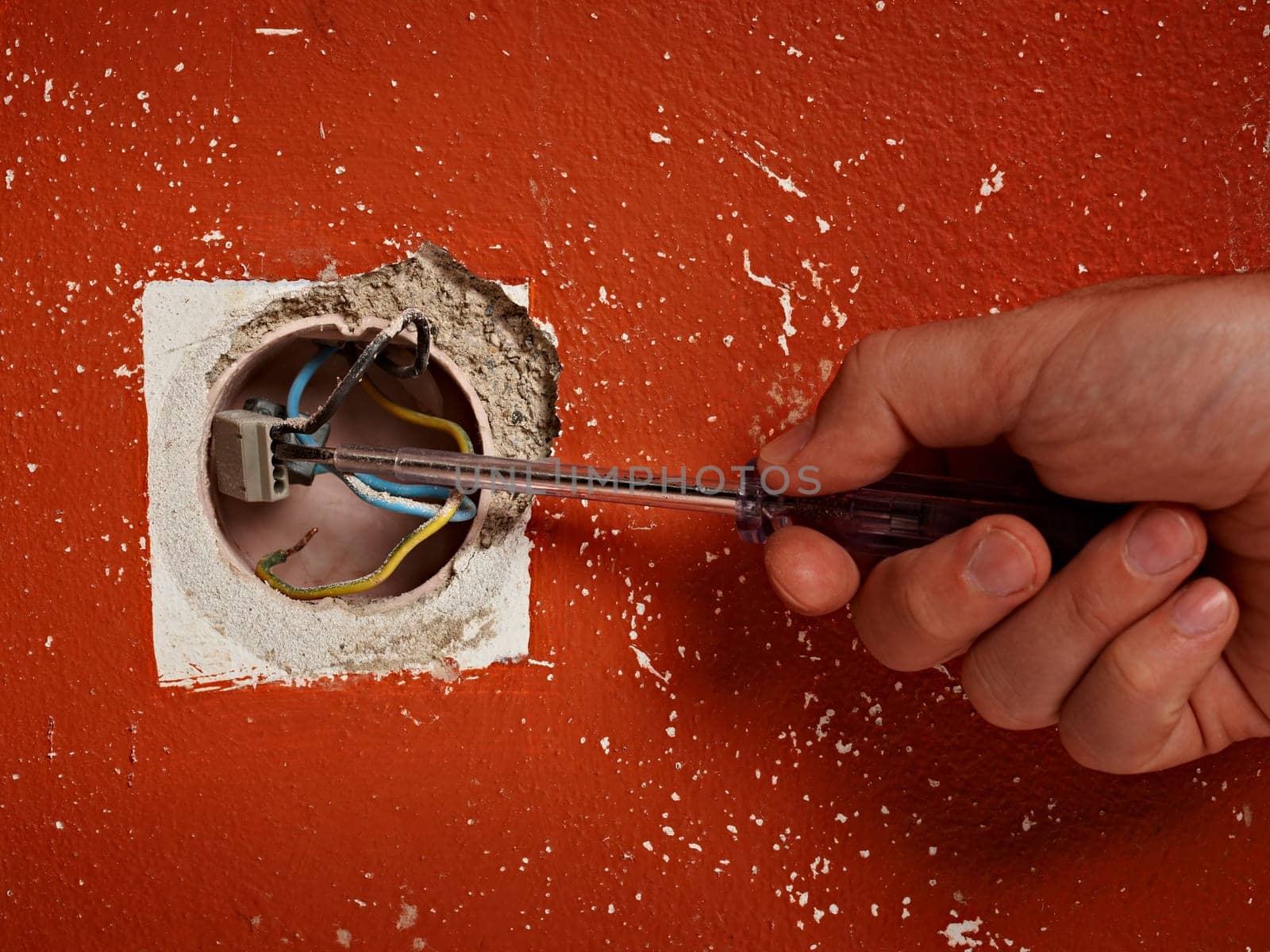 close up of hand holding a screwdriver in front of a electrical wall socket
