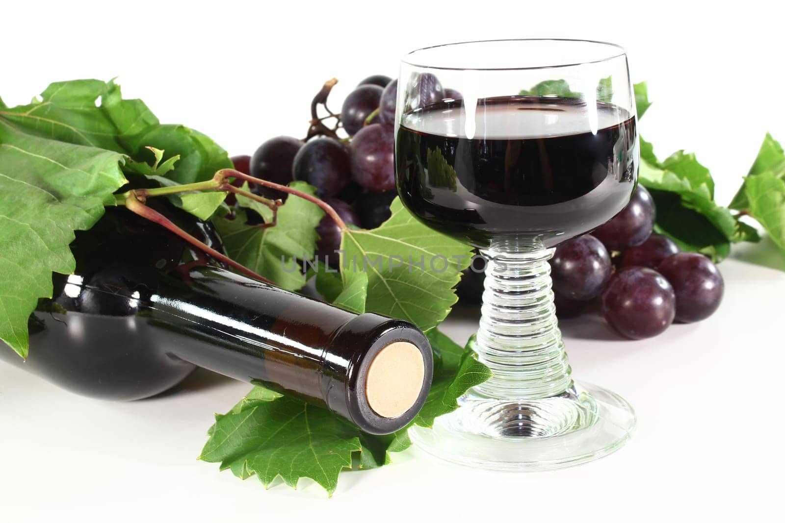 a bottle of red wine with glass, grapes and vine tendril on a white background