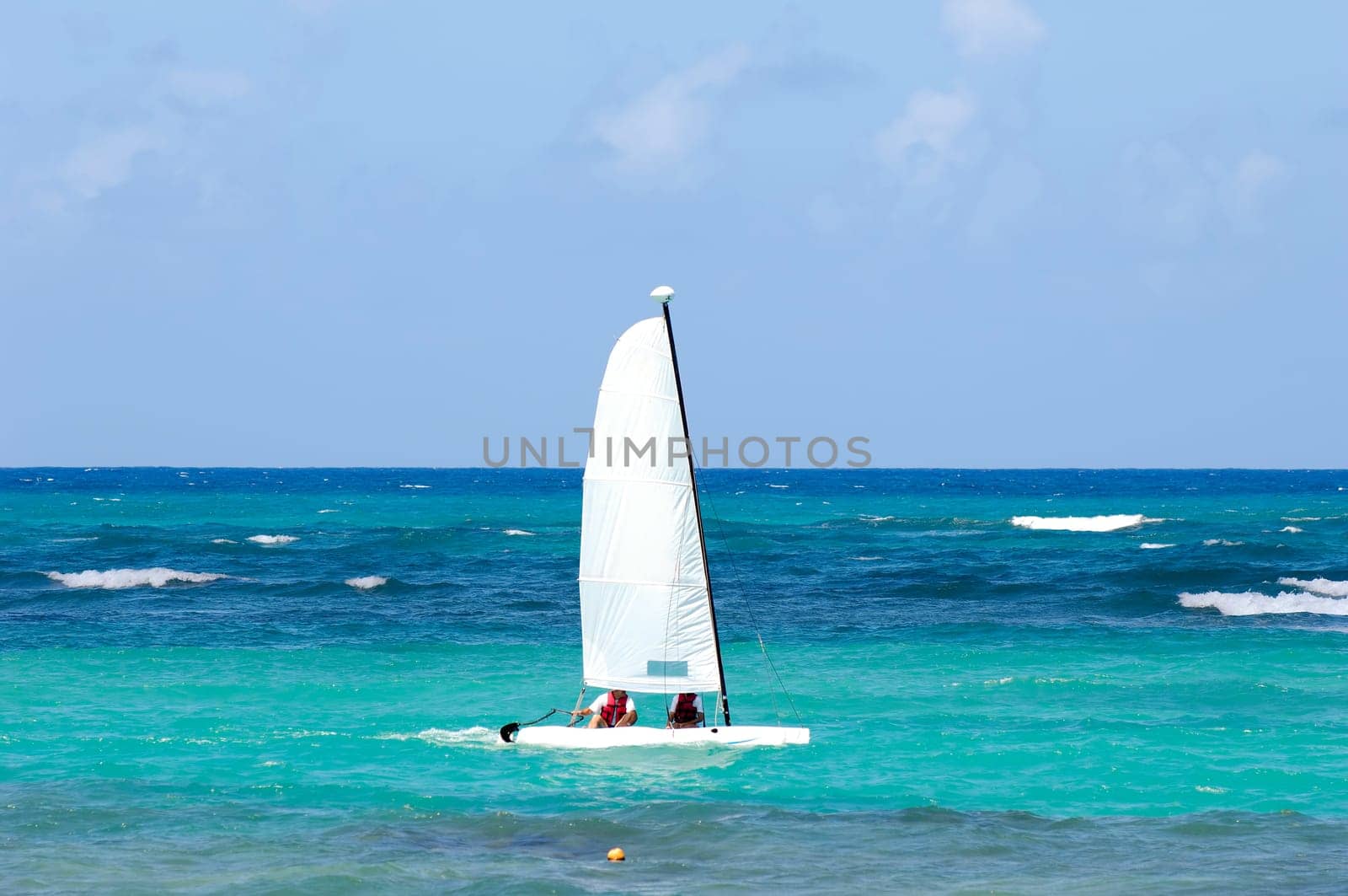 A sailboat is sailing on the blue caribbean sea.