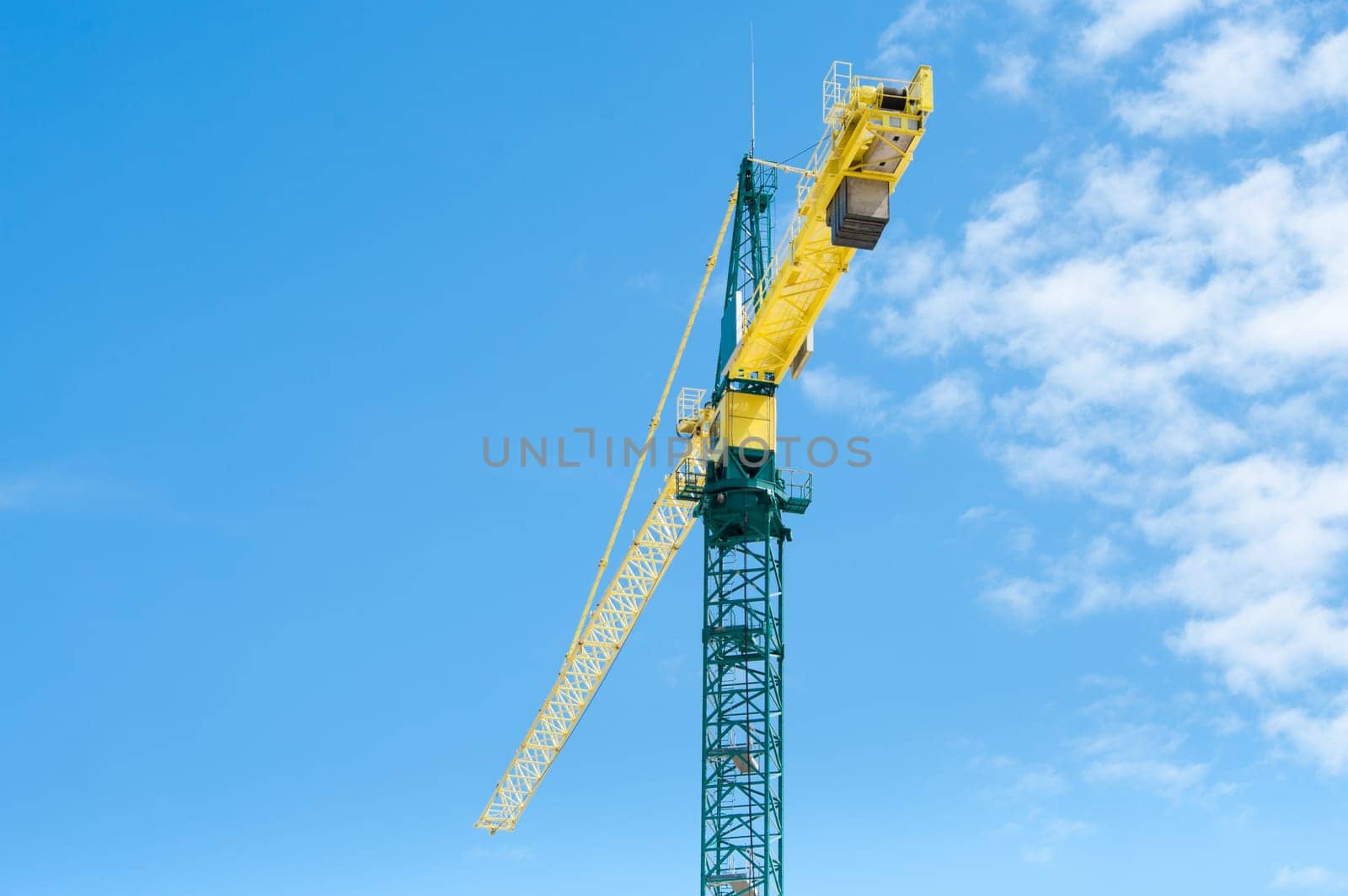 yellow with green crane against a partly clouded blue sky