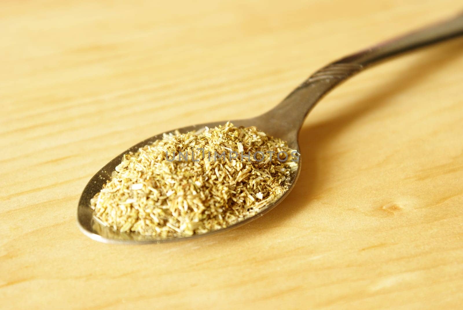 A teaspoon full of Chamomile tea over a wooden background.