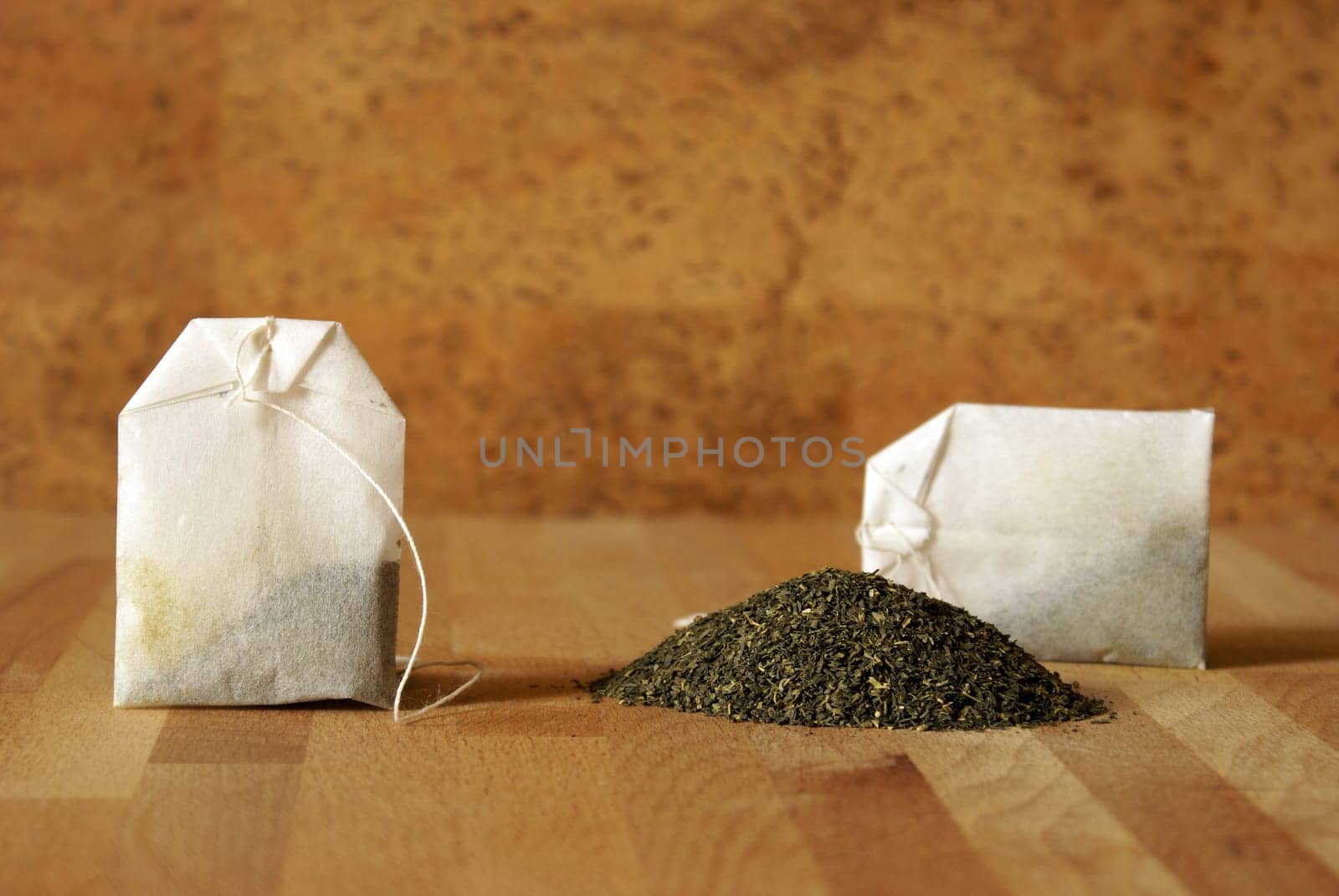 A couple of bags are next to a pile of green tea leaves.