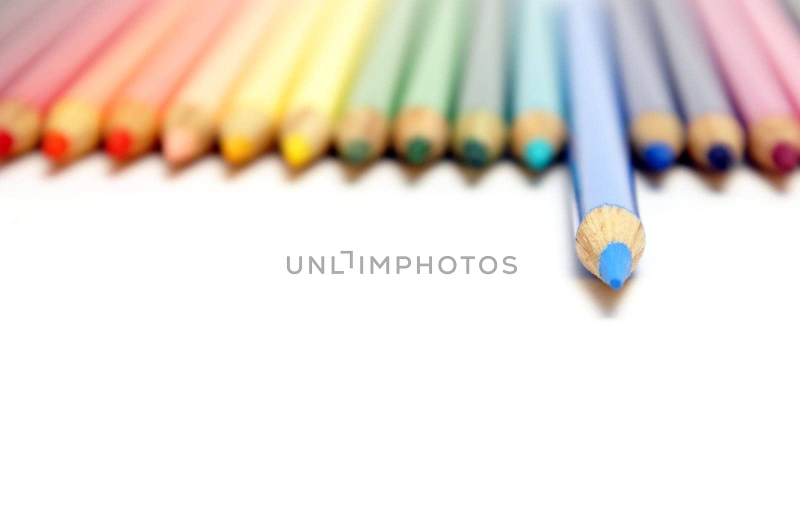 A spectrum of colored pencil crayons with a blue one ahead of the rest with a shallow depth of focus.