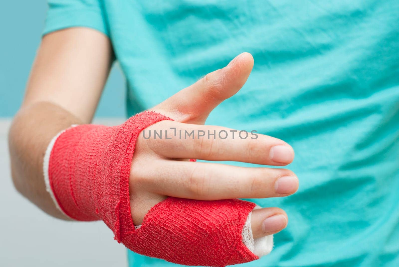 Injured male hand with upper part of body. Hand is bandaged with red plaster focus set on thumb