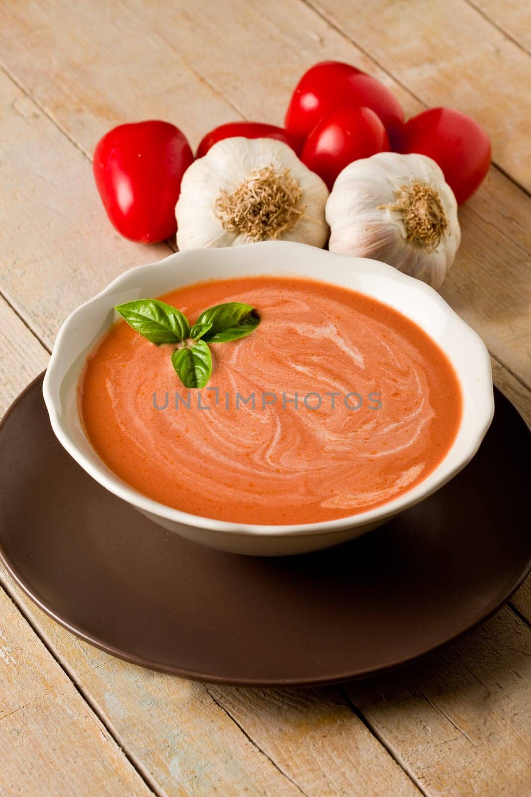photo of delicious tomato cream soup on wooden table with garlic and basil
