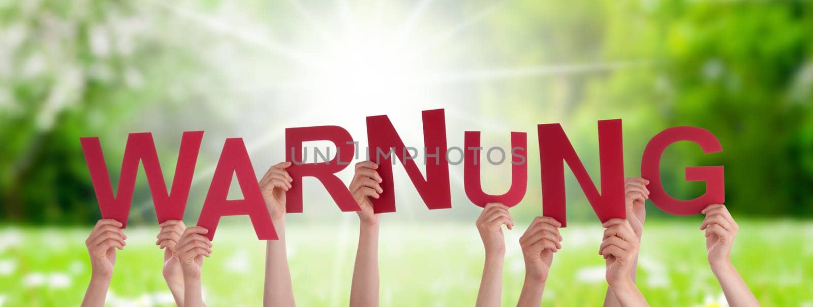 People Or Persons Hands Building German Word Warnung Means Warning. Sunny Green Grass Meadow As Background.