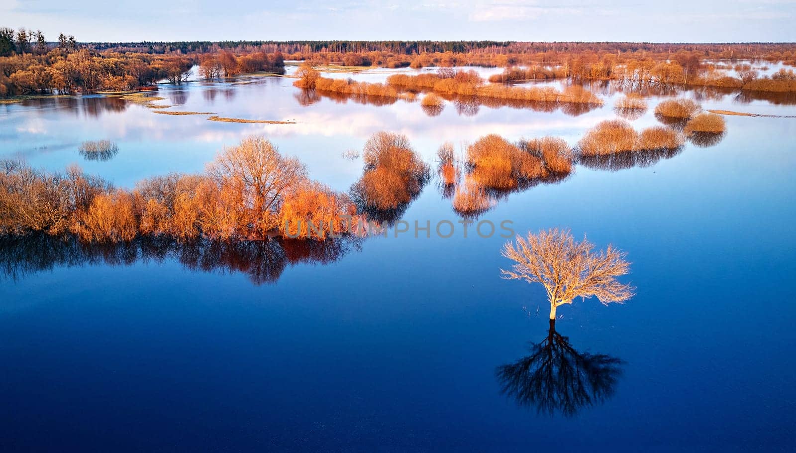 Spring flood rural landscape. Trees, meadow, bushes, fields, country road under High Water inundation. Sky, clouds reflection in evening light. Freshet Overflow aerial view. Floodplain area. Belarus