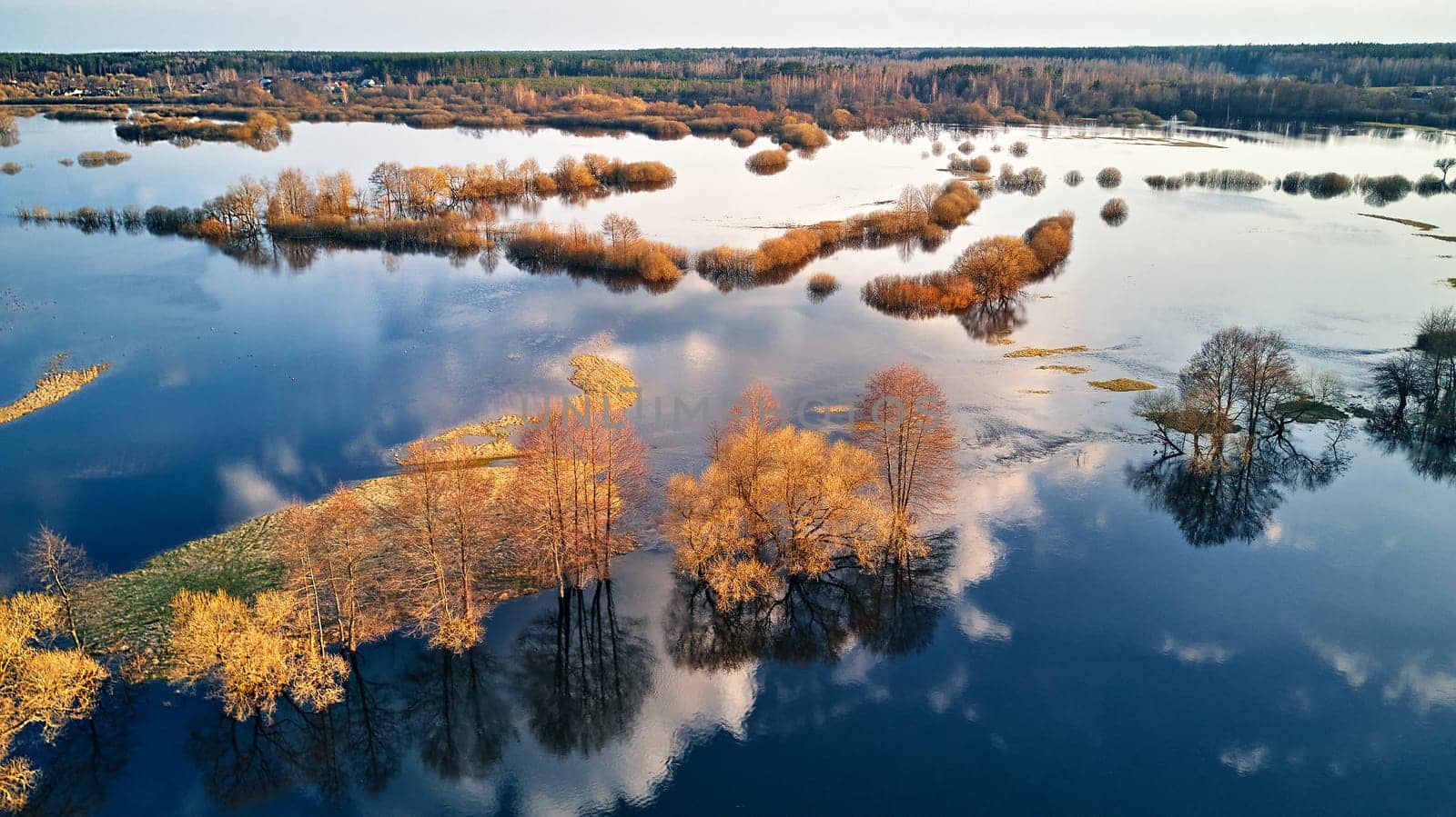 Spring flood rural landscape. Trees, meadow, bushes, fields, country road under High Water inundation. Sky and clouds reflection in evening light. Freshet Overflow aerial view. Floodplain area