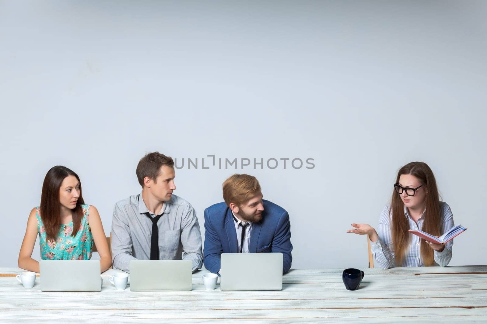 Business team working together at office on light gray background. all working on laptops. boss reading notebook. copyspace image