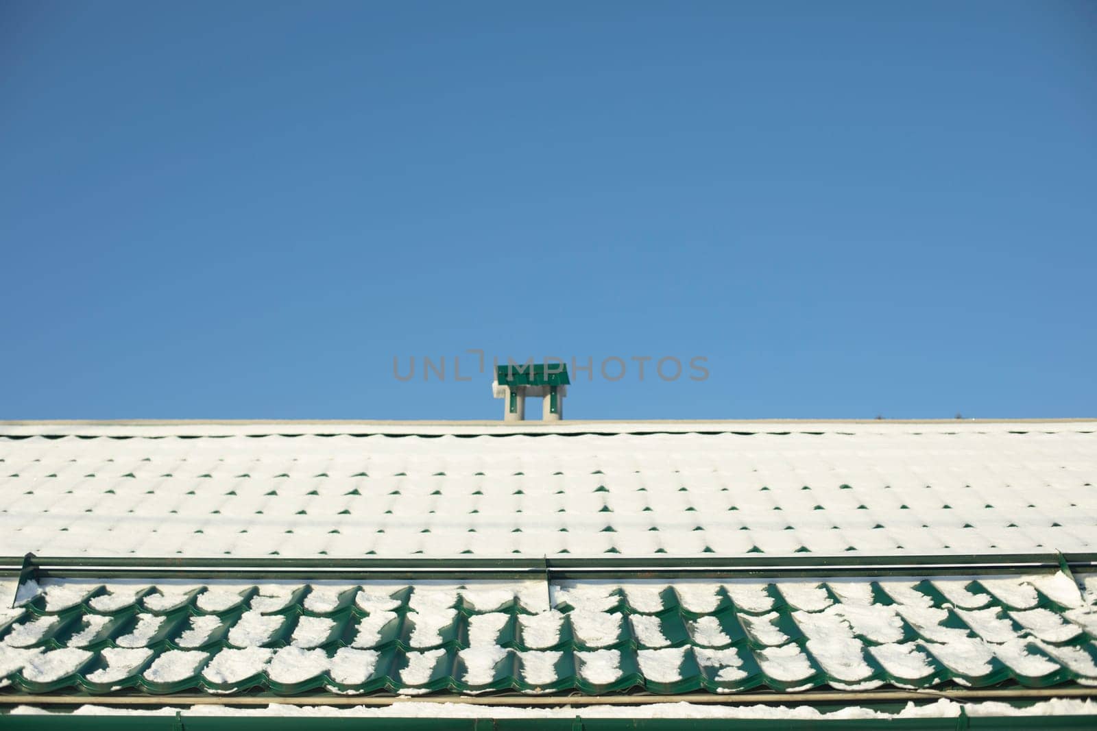 Roof in snow. Snow on roof. Details of house. Green prof flooring on building.