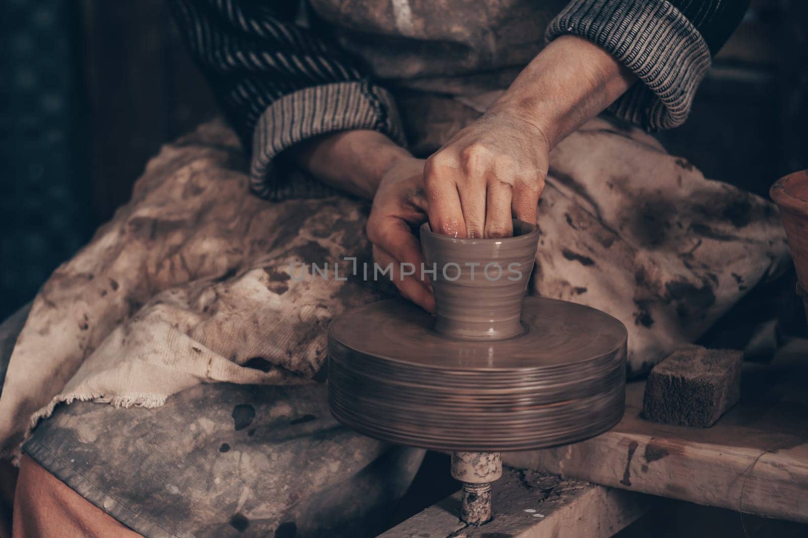 Modeling bowl from clay on wheel in pottery workshop. Dirty hands of craftsman mold crockery. Technique of crafting clayware. Working on potter wheel with raw clay, shaping pot. Traditional crafting.