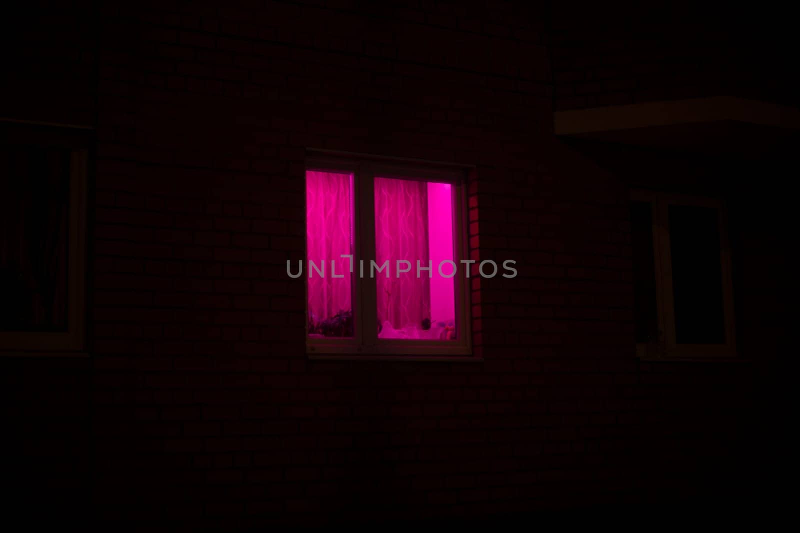Rose window at night. Pink light in house. Bright color.