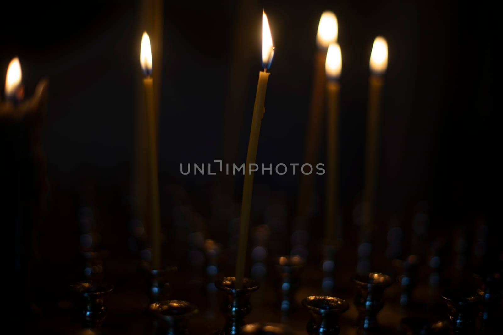 Candles burn in dark. Flames from randomly painted wax candles. Fire on black background. Religious rite.