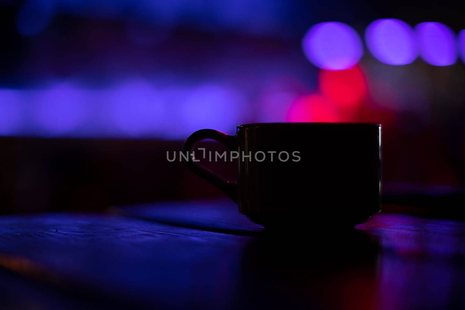 Cup on table in bar. Coffee mug in restaurant. Drink cup in purple light. Interior details. Blurred background.