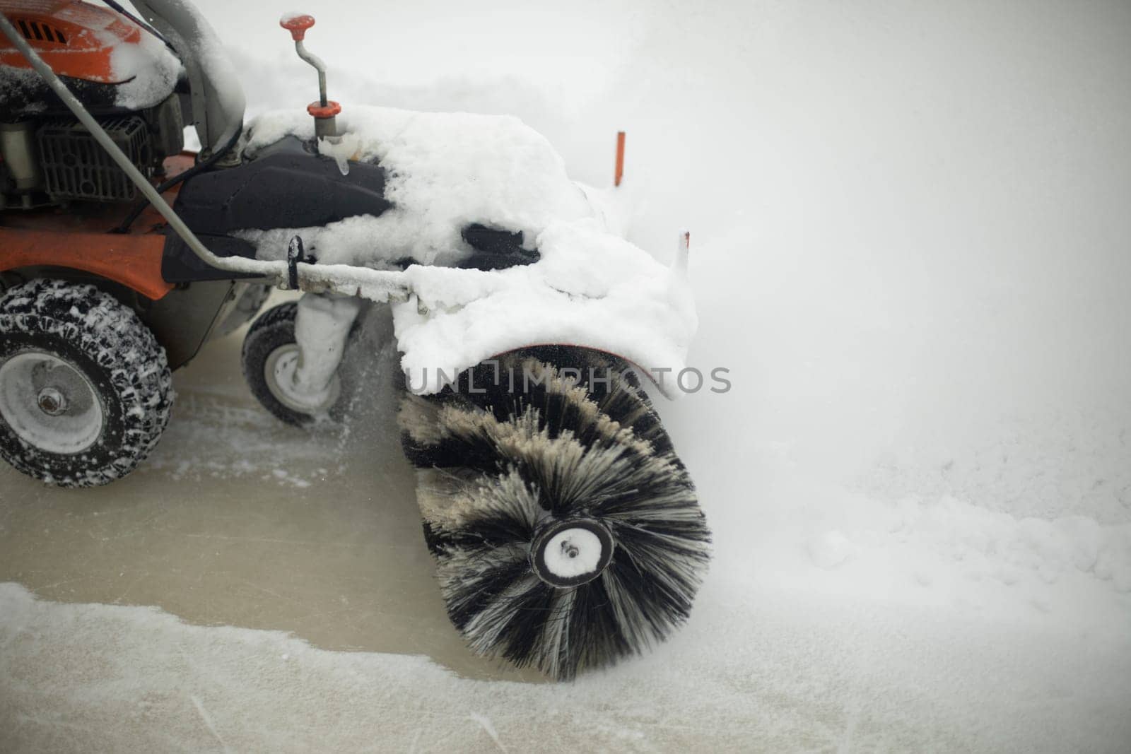 Snow removal equipment on street. Brush cleans snow. Ice preparation at rink. Rotation of brush from plastic pile.