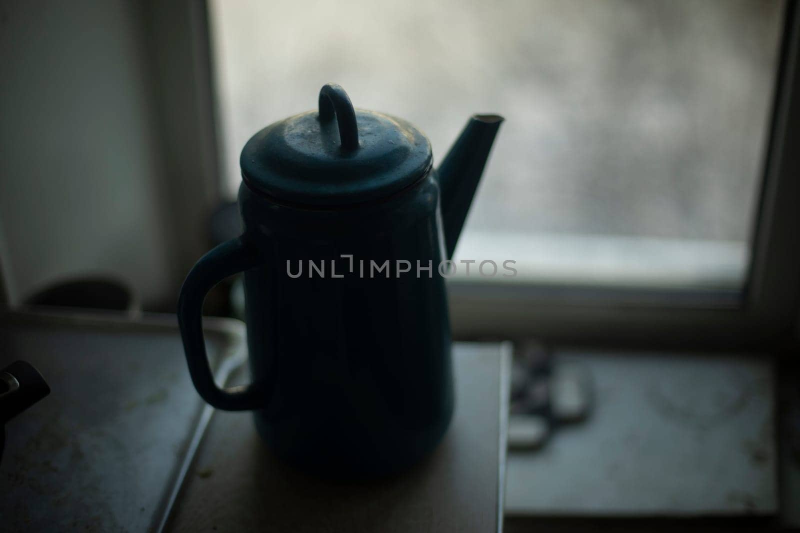Kettle on background of window. Kettle with handle. Silhouette of kitchen utensils. Kitchen details.