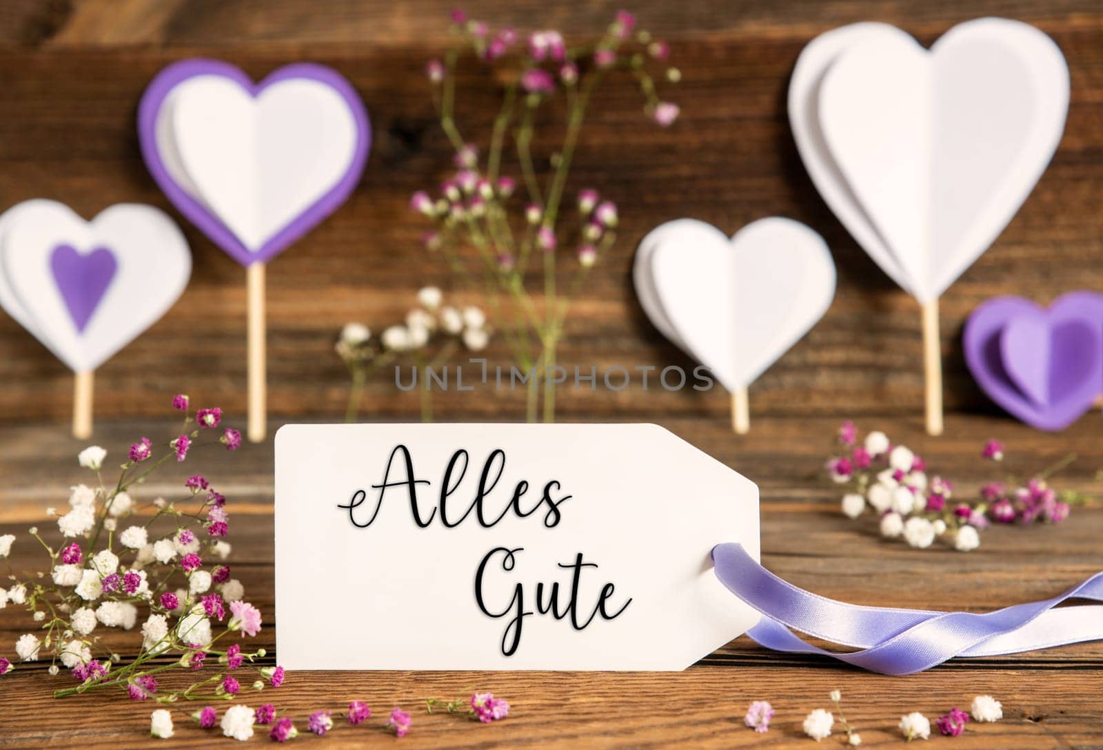Label With German Text Alles Gute Means Best Wishes. Purple And Lilac Decoration And Spring Flower Arrangement. Heart Symbols With Wooden Background.