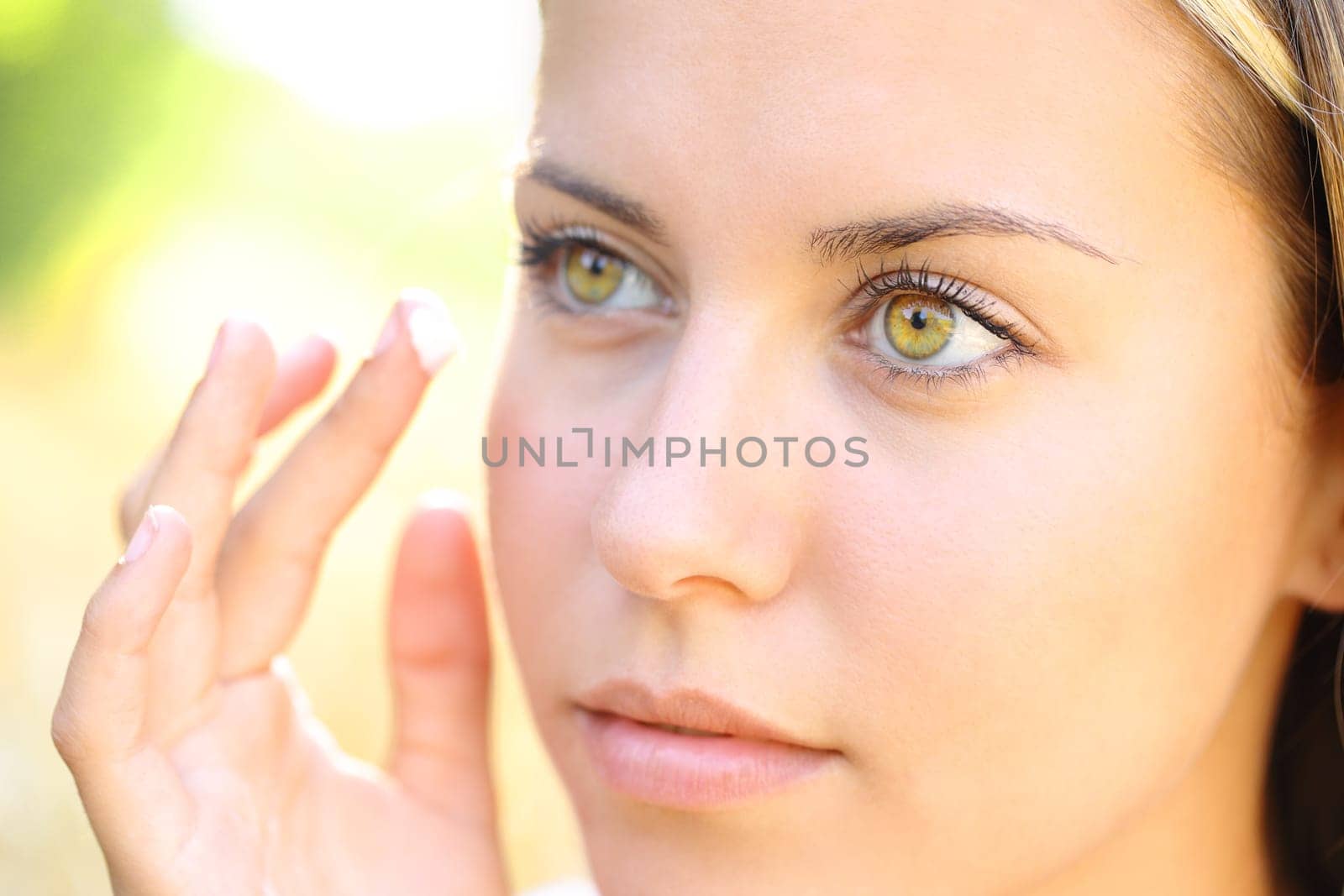 Close up portrait of a beauty woman hand applying moisturizer on face in nature