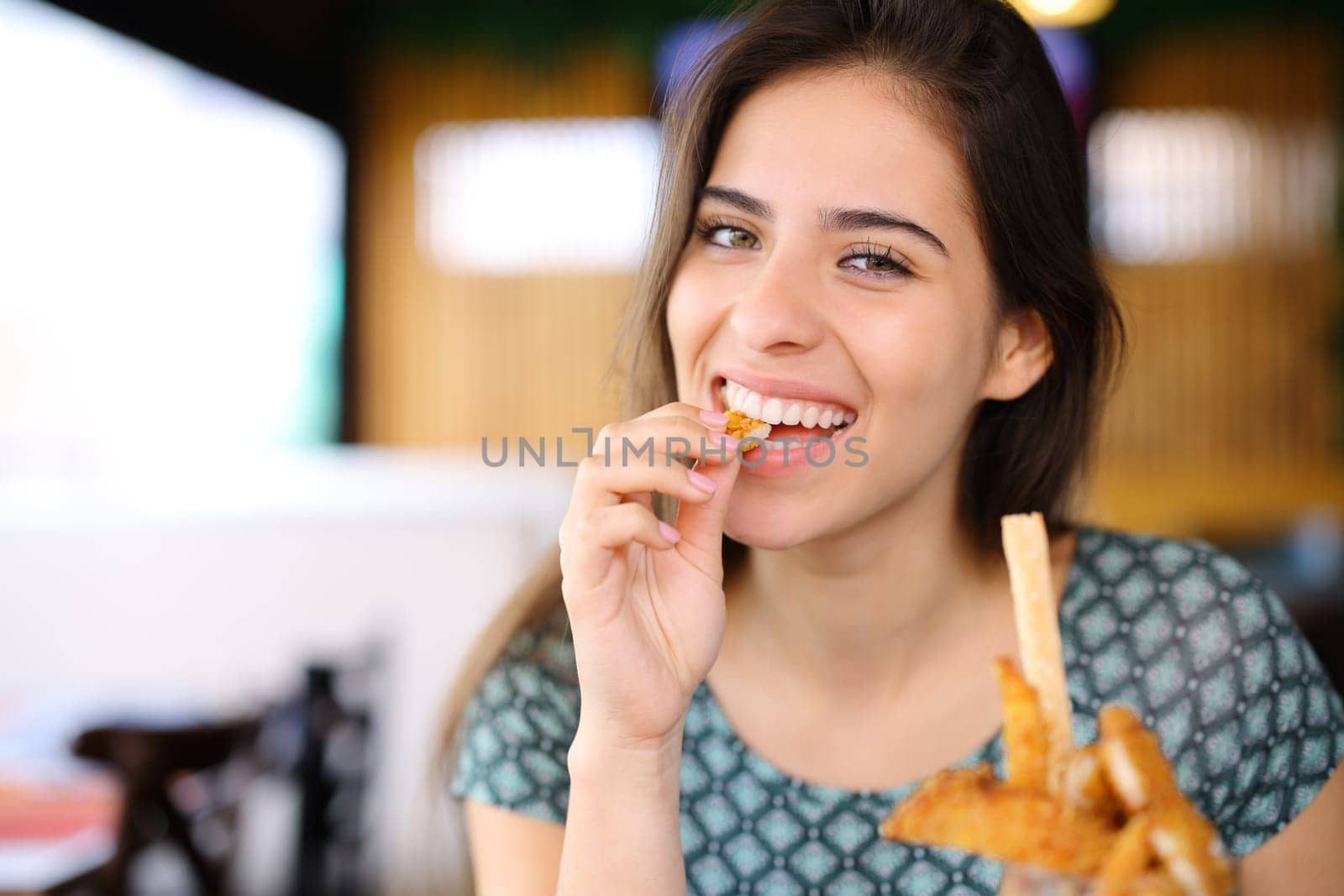 Happy woman eating chicken fingers looking at camera in a restaurant