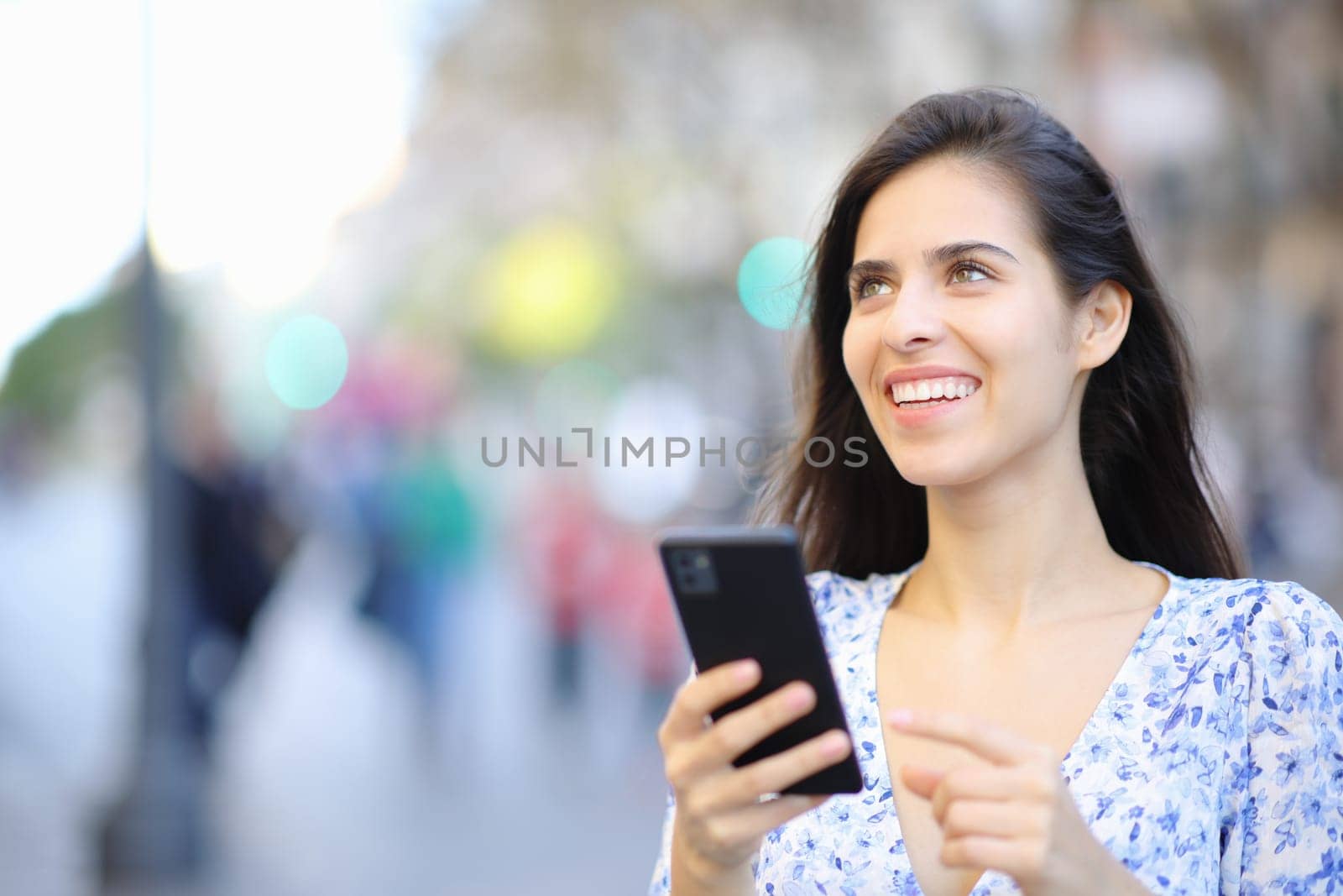 Happy woman holding cell phone looks up in the street