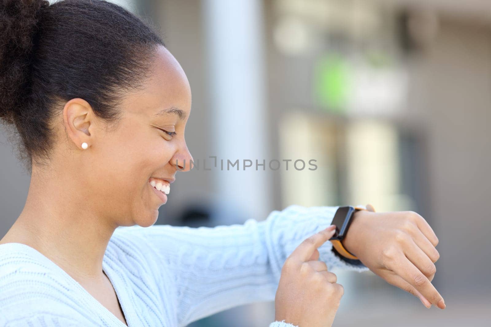 Profile of a happy black woman checking smartwatch in the street