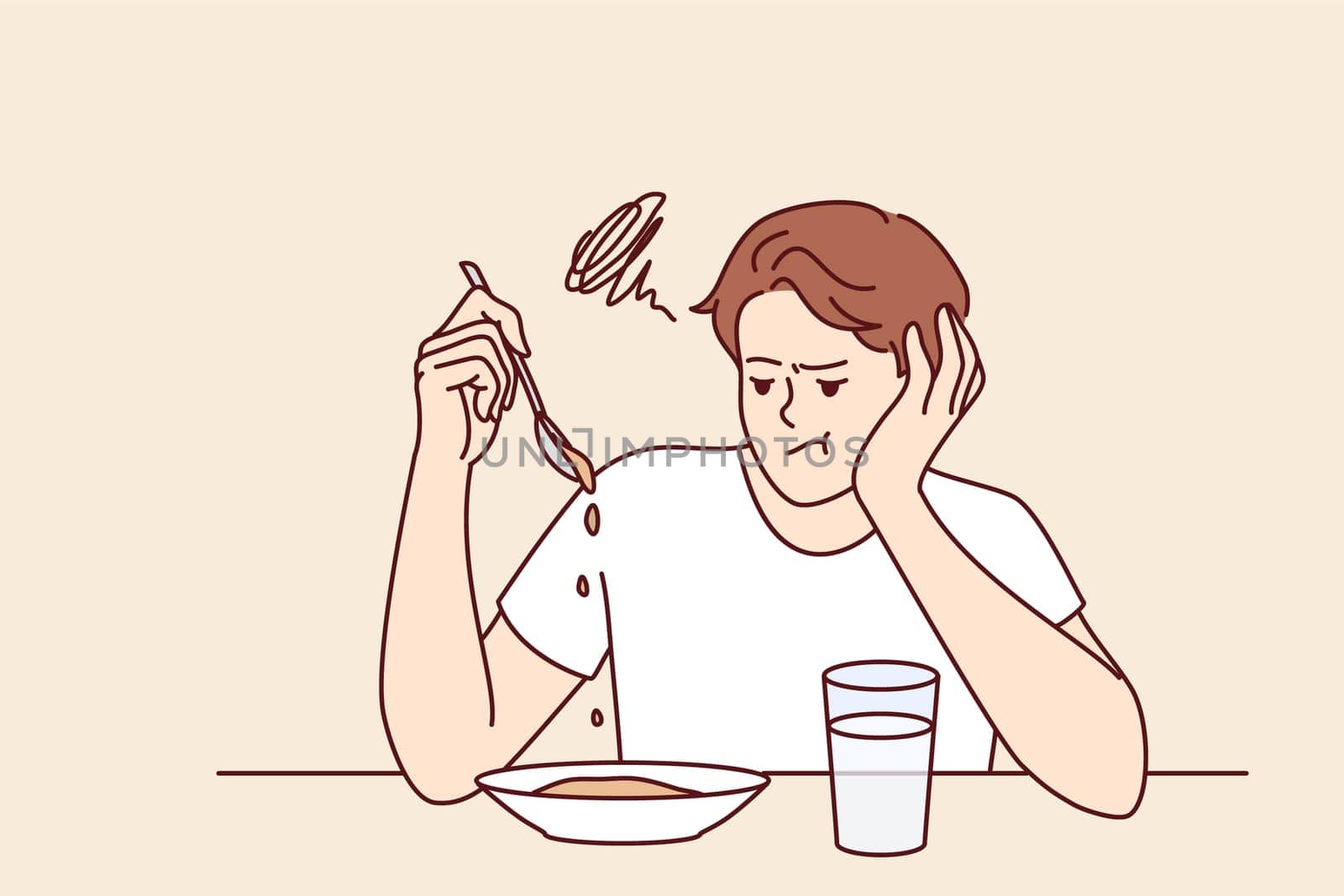 Man suffers from lack of appetite sitting at table in kitchen and does not want to eat breakfast. Depressed guy with unhappy expression melancholy looks at plate with not appetite food during diet