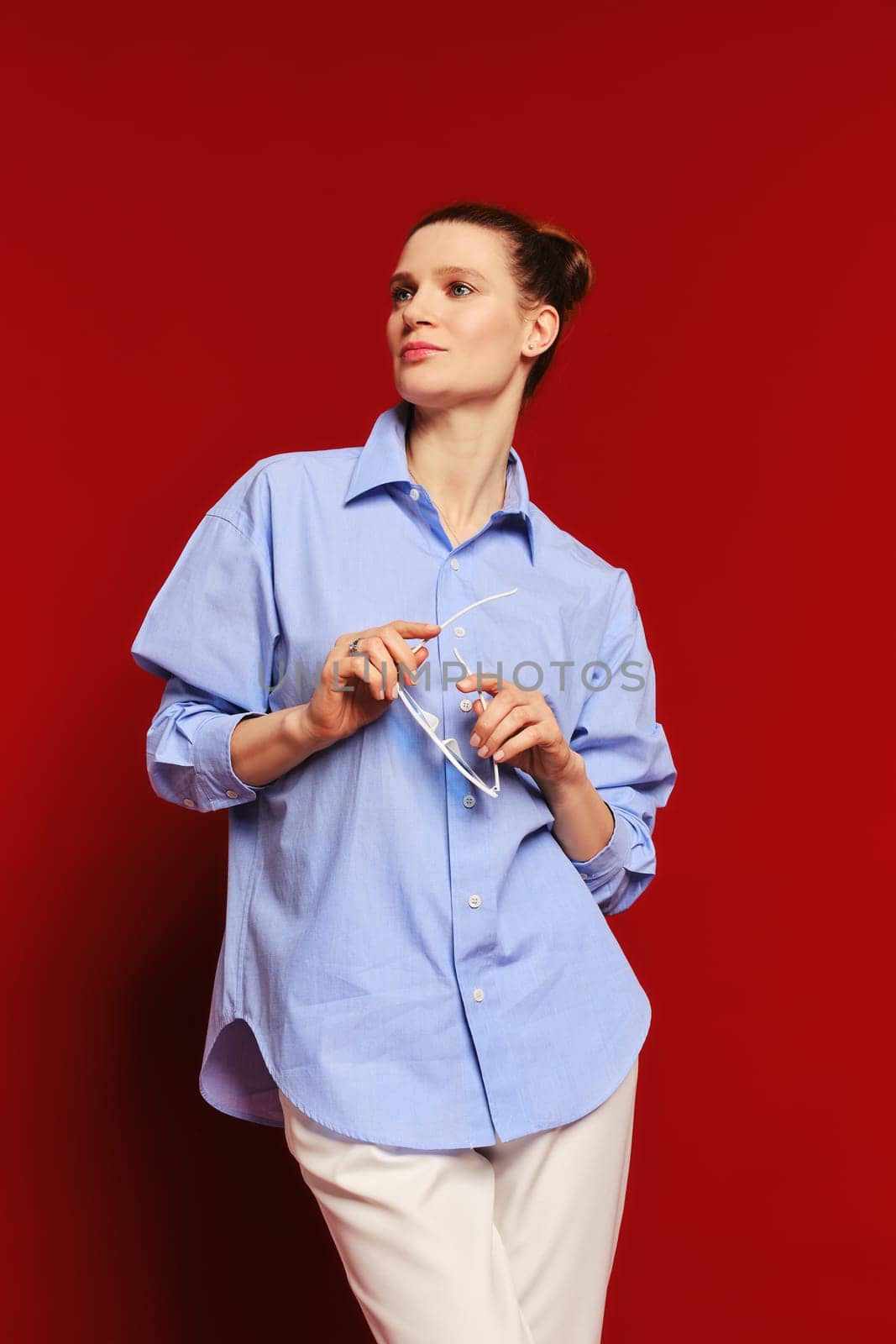 Low angle view of classy woman in cotton shirt and trousers holding in hands her sunglasses