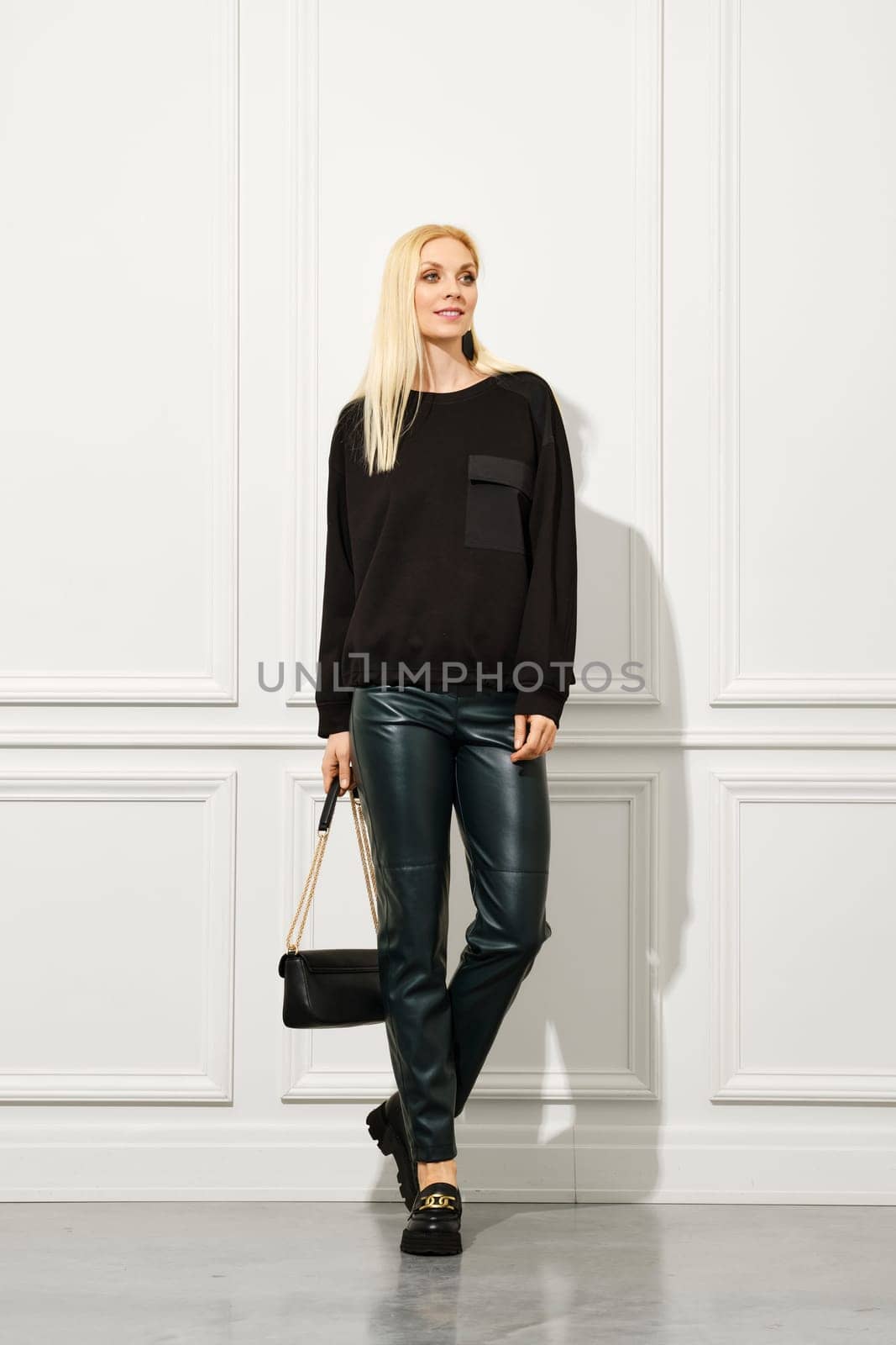 Cute woman in trendy urban outfit with hand bag walks in bright room