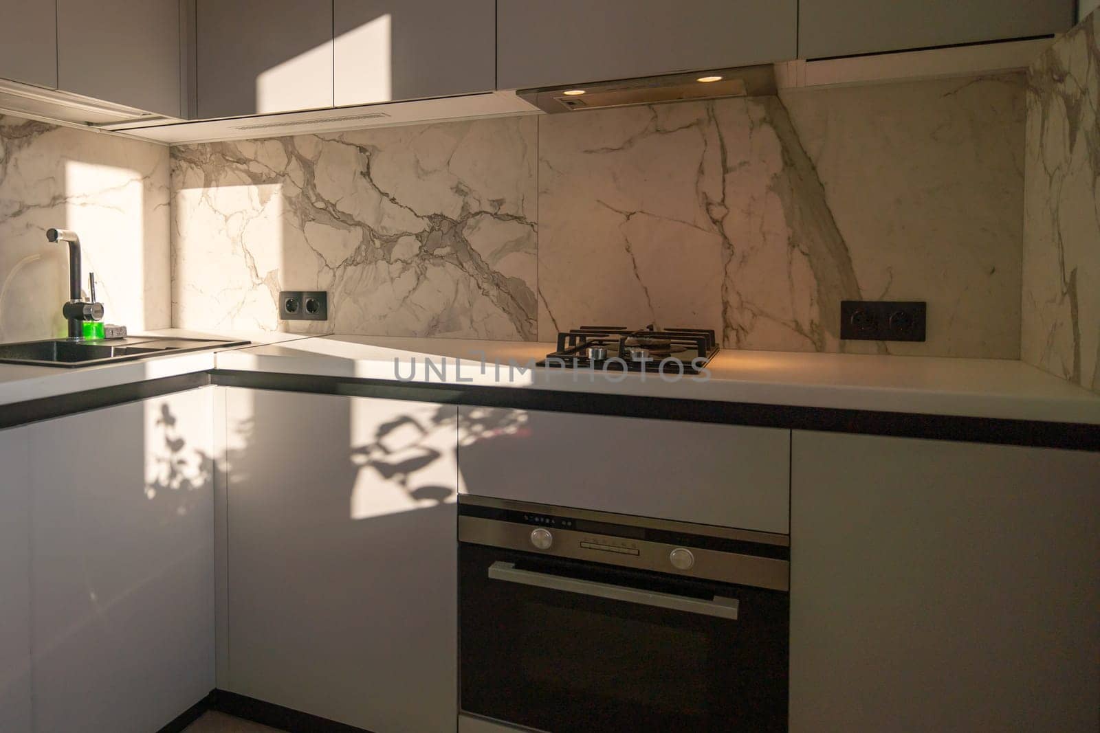 Modern kitchen with marble backsplash, built-in oven, gas cooktop, and sleek gray cabinetry. Sunlight streams in.