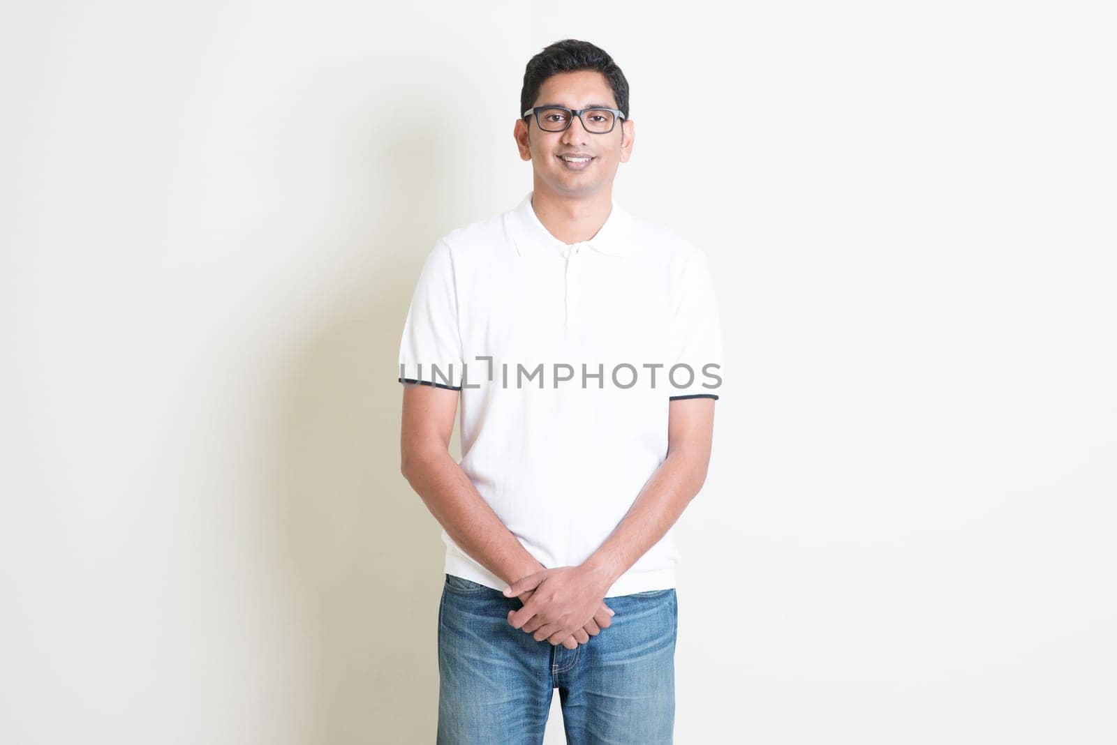 Front view portrait Indian guy standing on plain background with shadow and copy space.