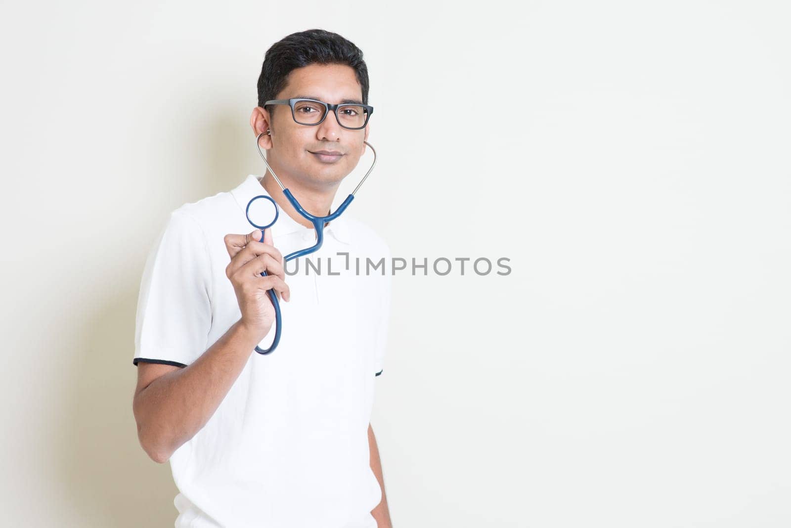 Indian medical student with stethoscope in hand. Asian man standing on plain background with shadow and copy space. Handsome male model.