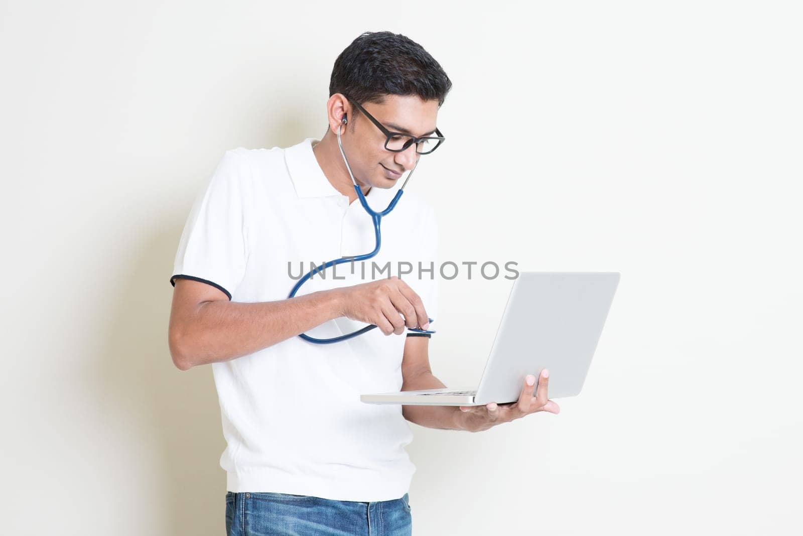 Spyware or malware concept. Indian computer engineer diagnose virus infected pc with stethoscope. Asian man standing on plain background with shadow and copy space.