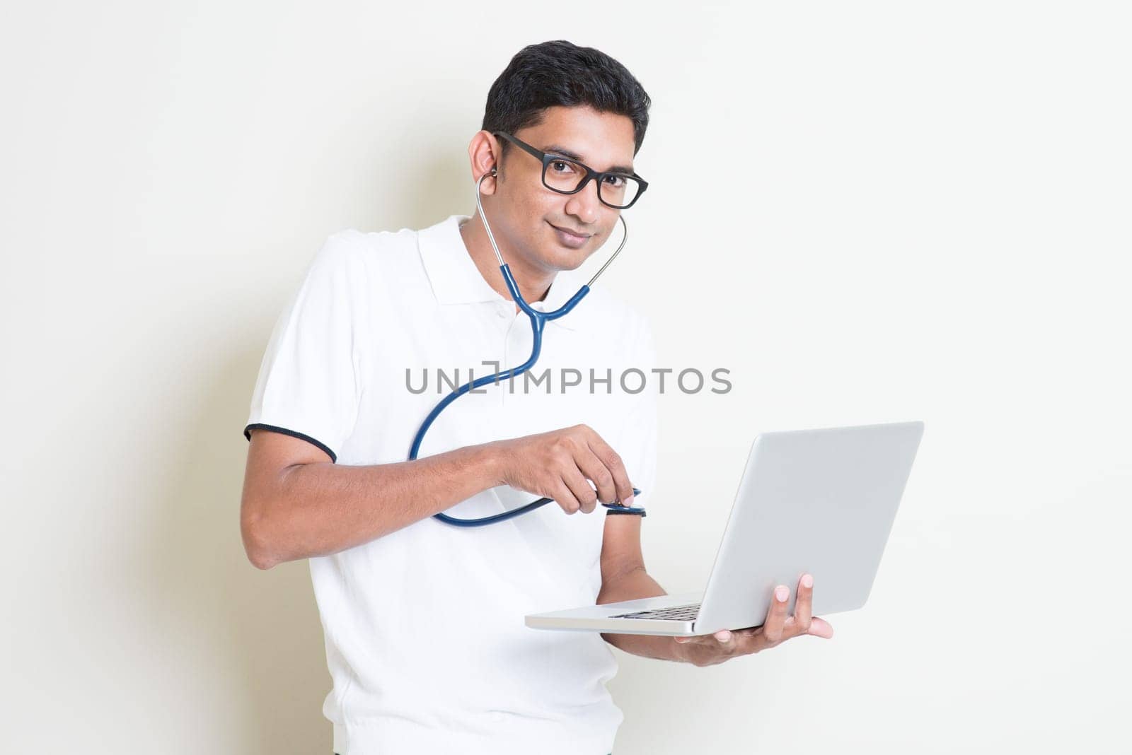 Antivirus concept. Indian computer engineer diagnose virus infected pc with stethoscope. Asian man standing on plain background with shadow and copy space.