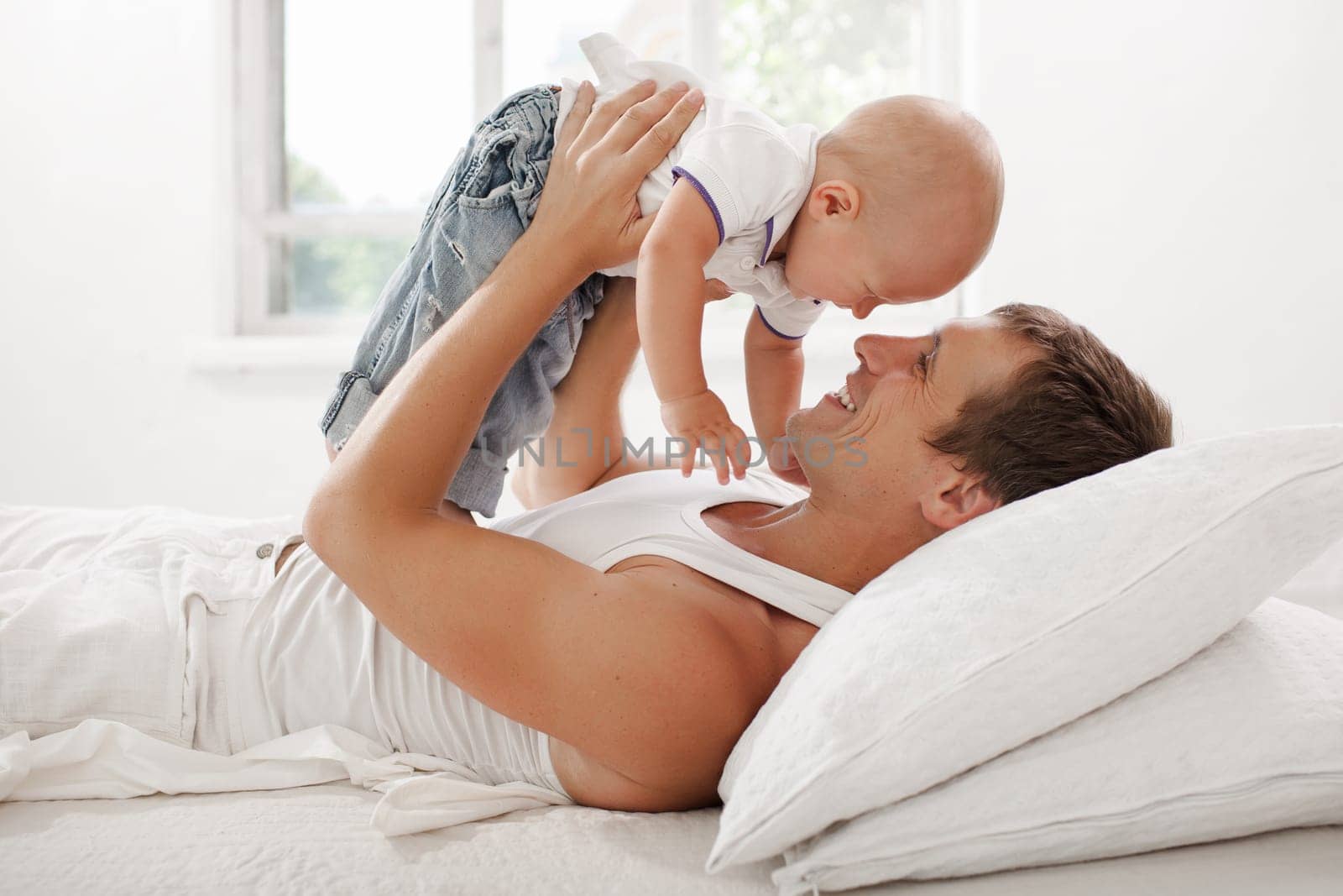 young father with his nine months old som on the bed at home on white background