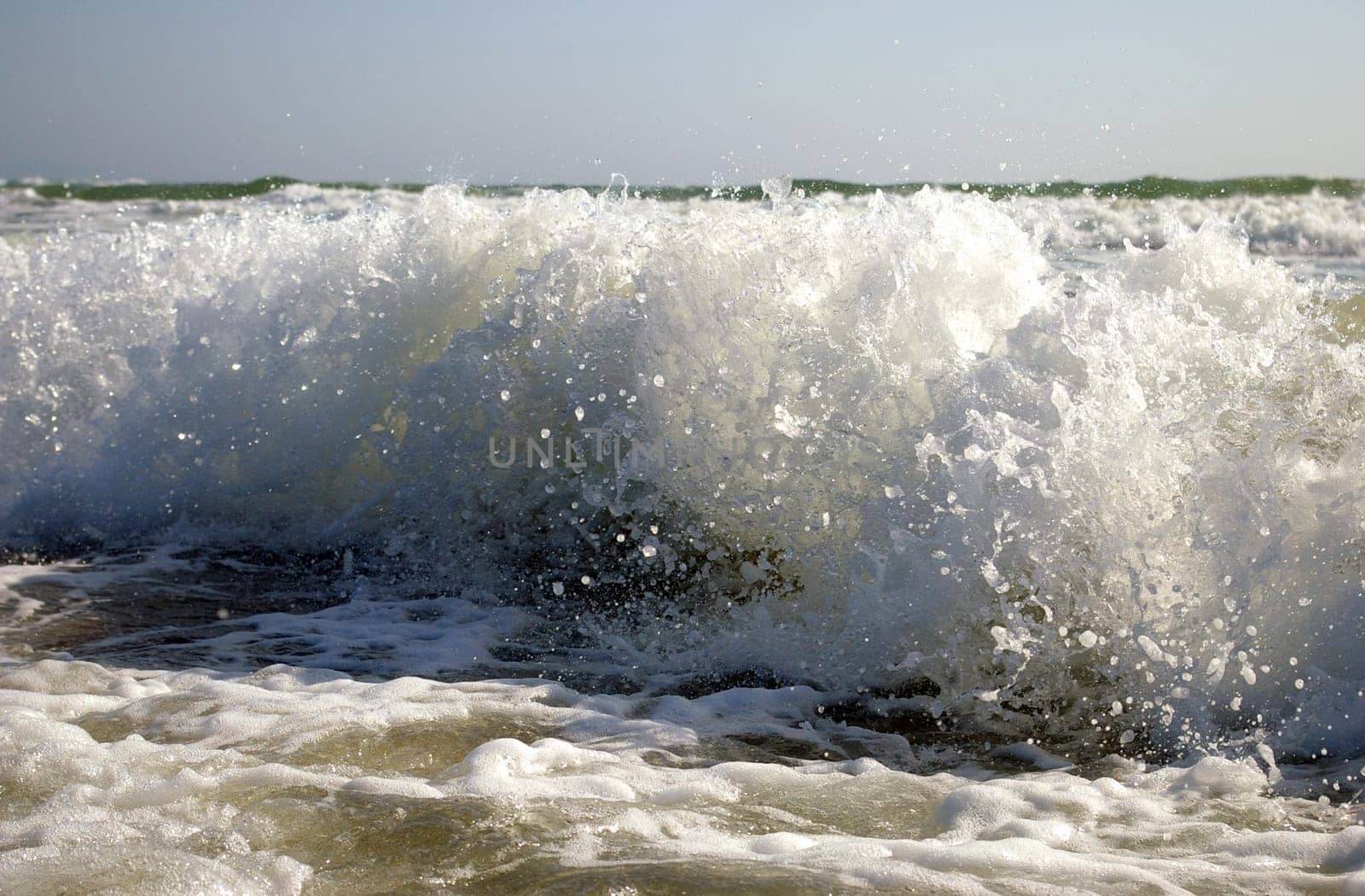 Blanching spume of the sea wave wears down on sandy coast.