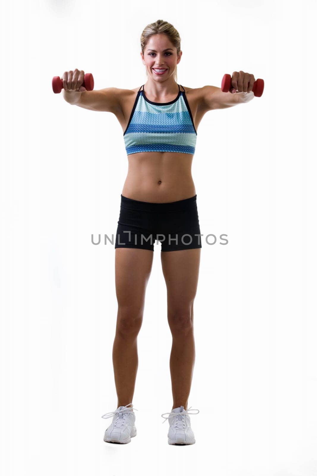 Full body of an attractive blond woman in great physical shape wearing black shorts and workout top standing on white with raised arms holding three pound weights