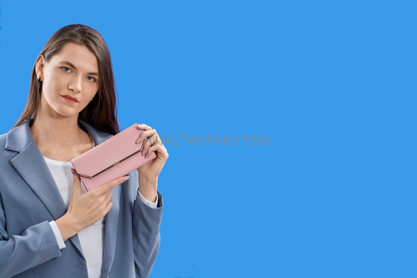 A beautiful young woman is holding a pink purse on a blue background, copy space. High quality photo