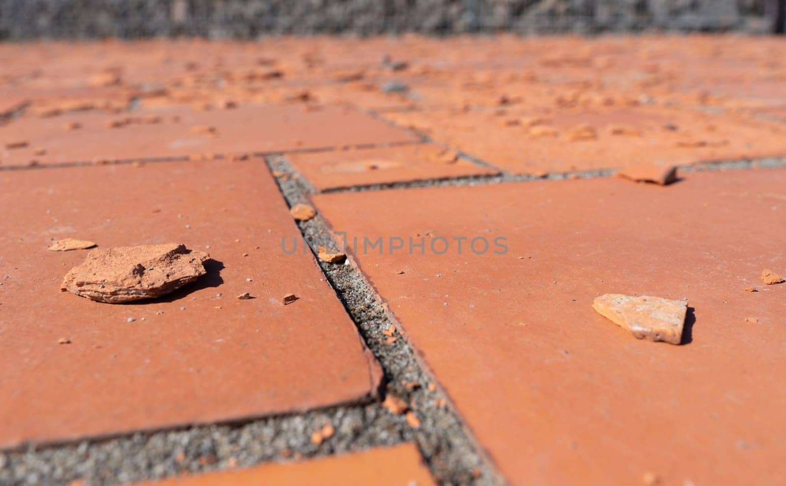 Red square floor tiles damaged by weathering or material defects. The surface is crumbling and the plates are disintegrating.