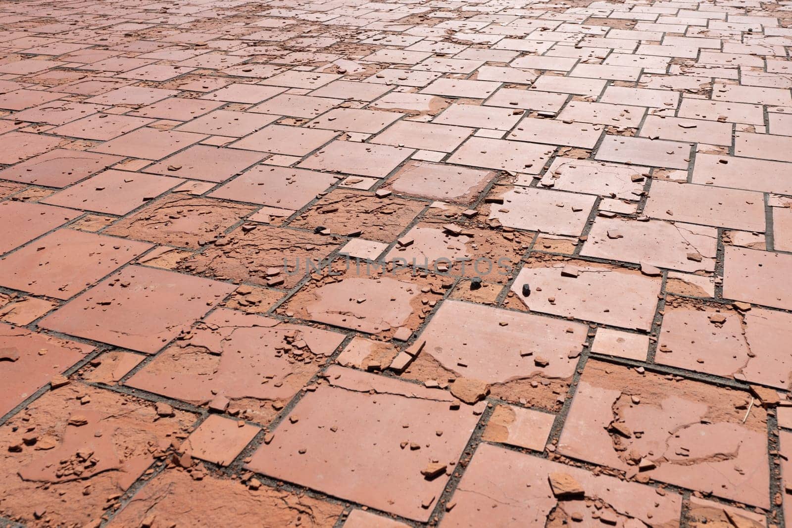 Red square floor tiles damaged by weathering or material defects. The surface is crumbling and the plates are disintegrating.