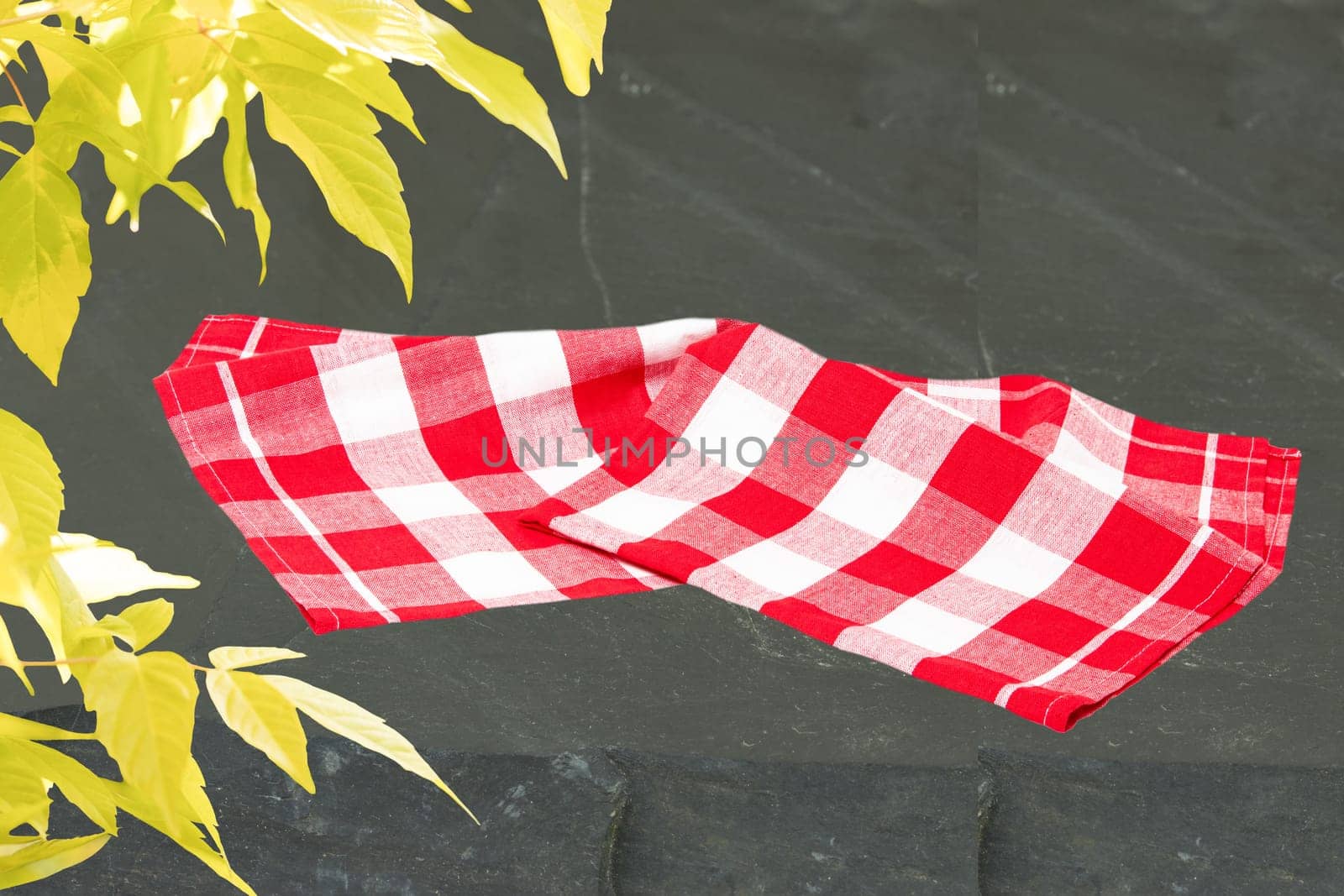 Empty red checkered tablecloth or napkin and yellow maple in spring on slate plate. Space for your food and product display montage. Recipe concept.