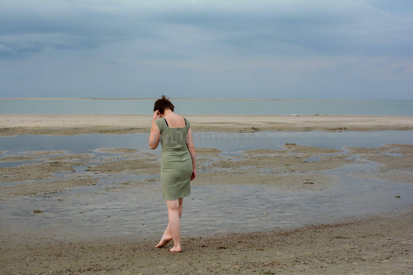 Young woman in a short green dress is standing in front of the sea on a sandy beach