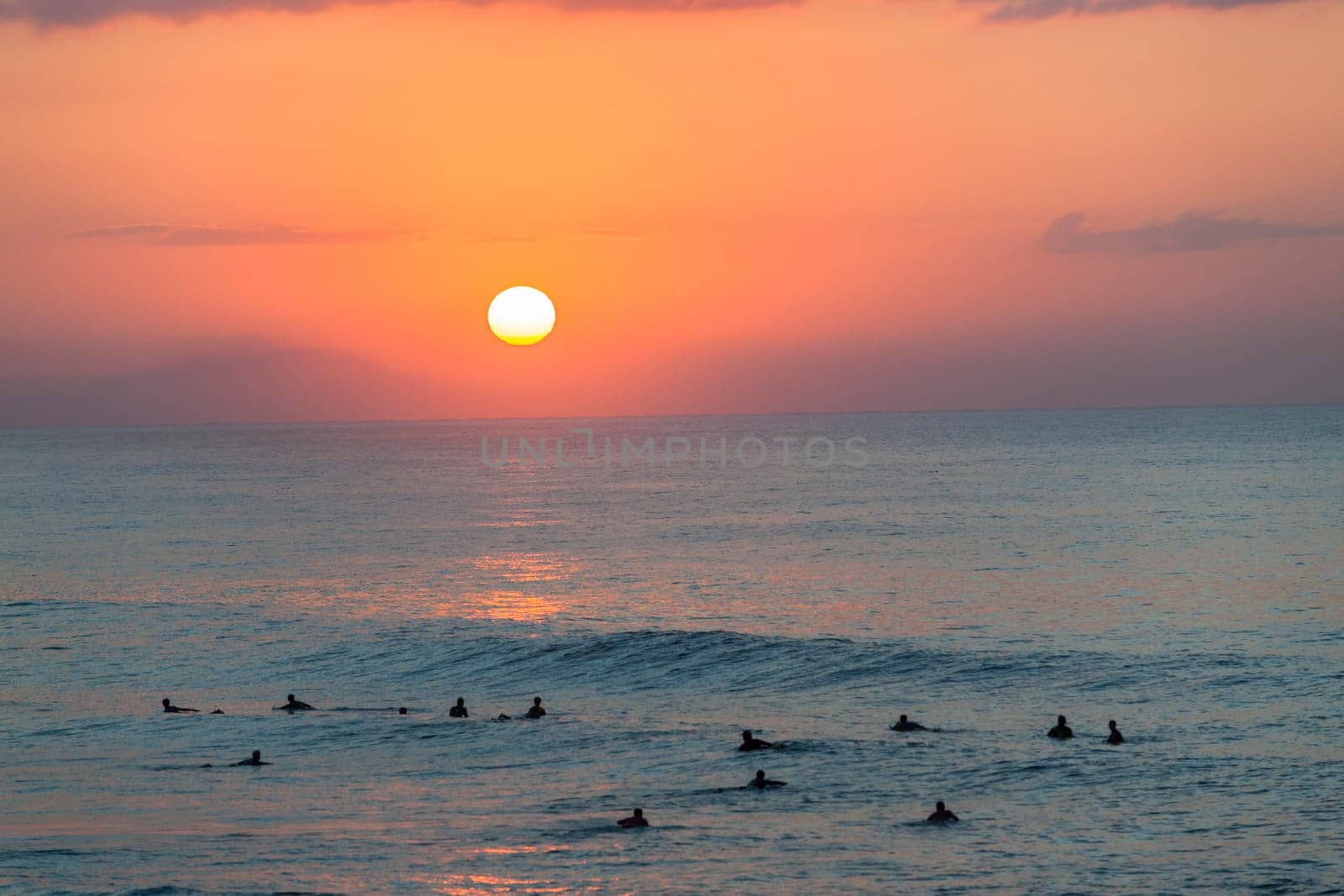 Surfing surfers in ocean wave waters early dawn sunrise on the horizon.