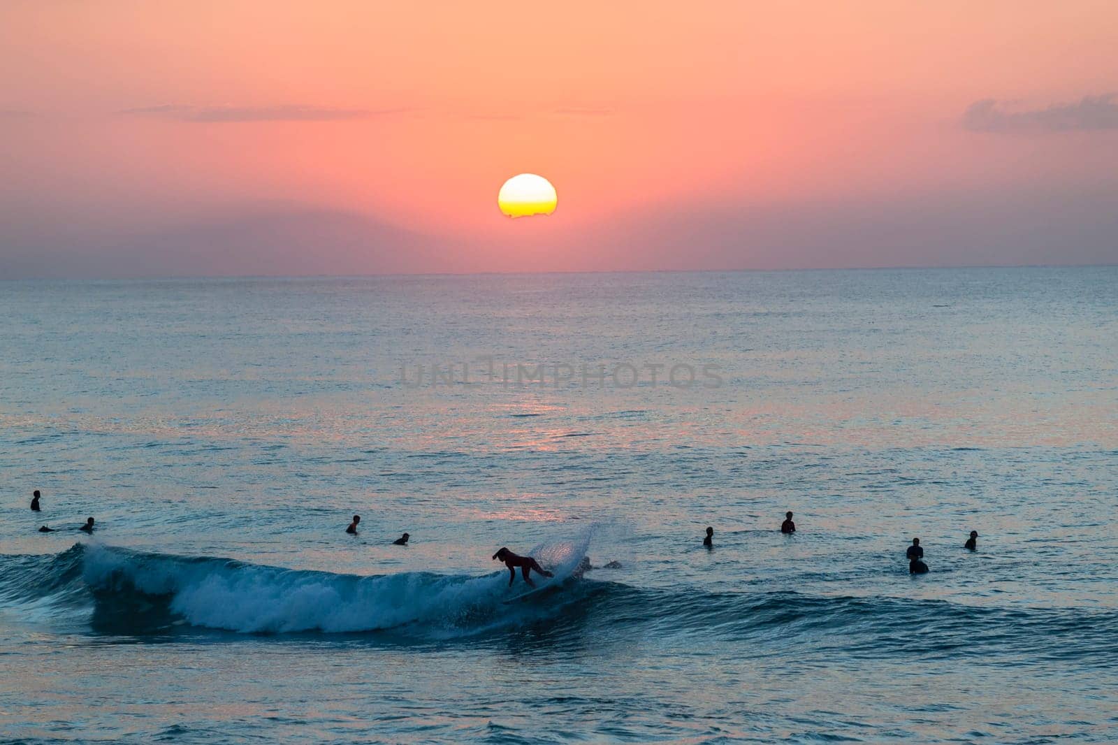 Surfing surfers in ocean wave waters early dawn sunrise on the horizon.