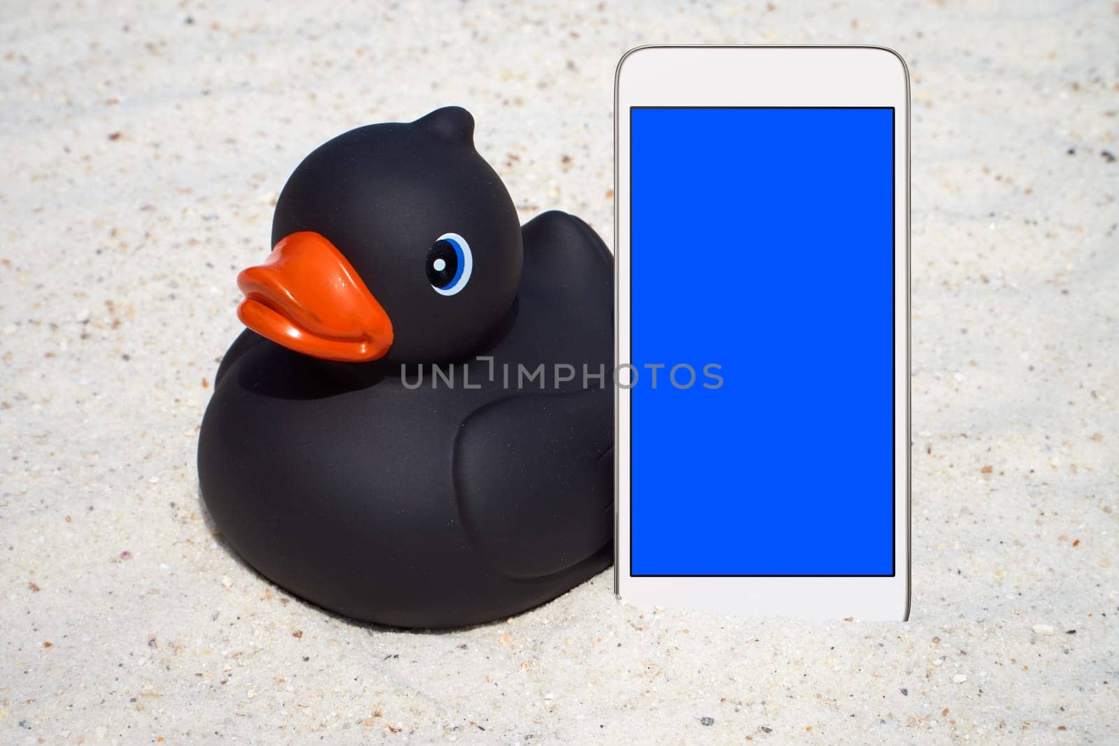 Black rubber duck and smartphone on the beach