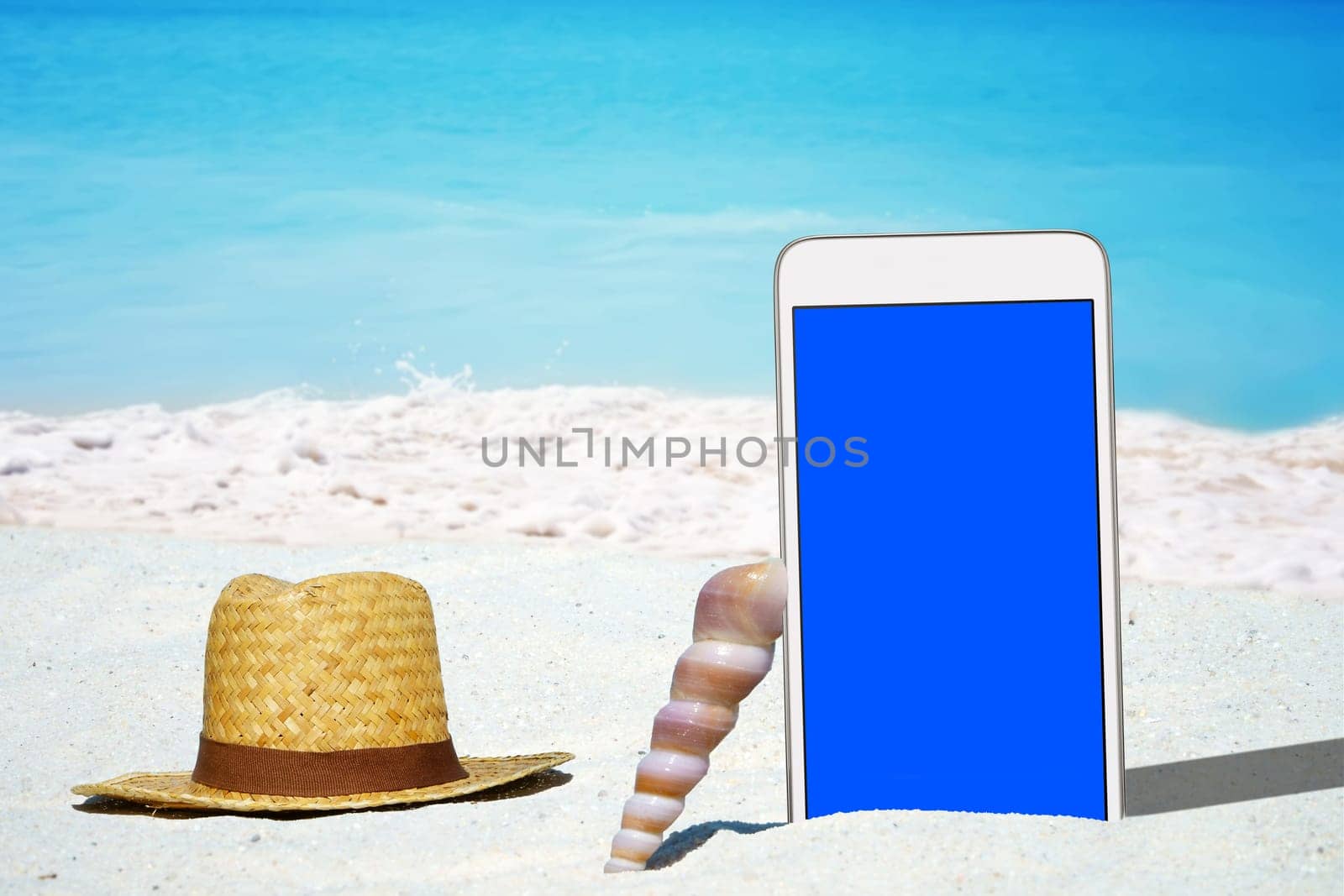White smartphone and straw hat on the sandy beach