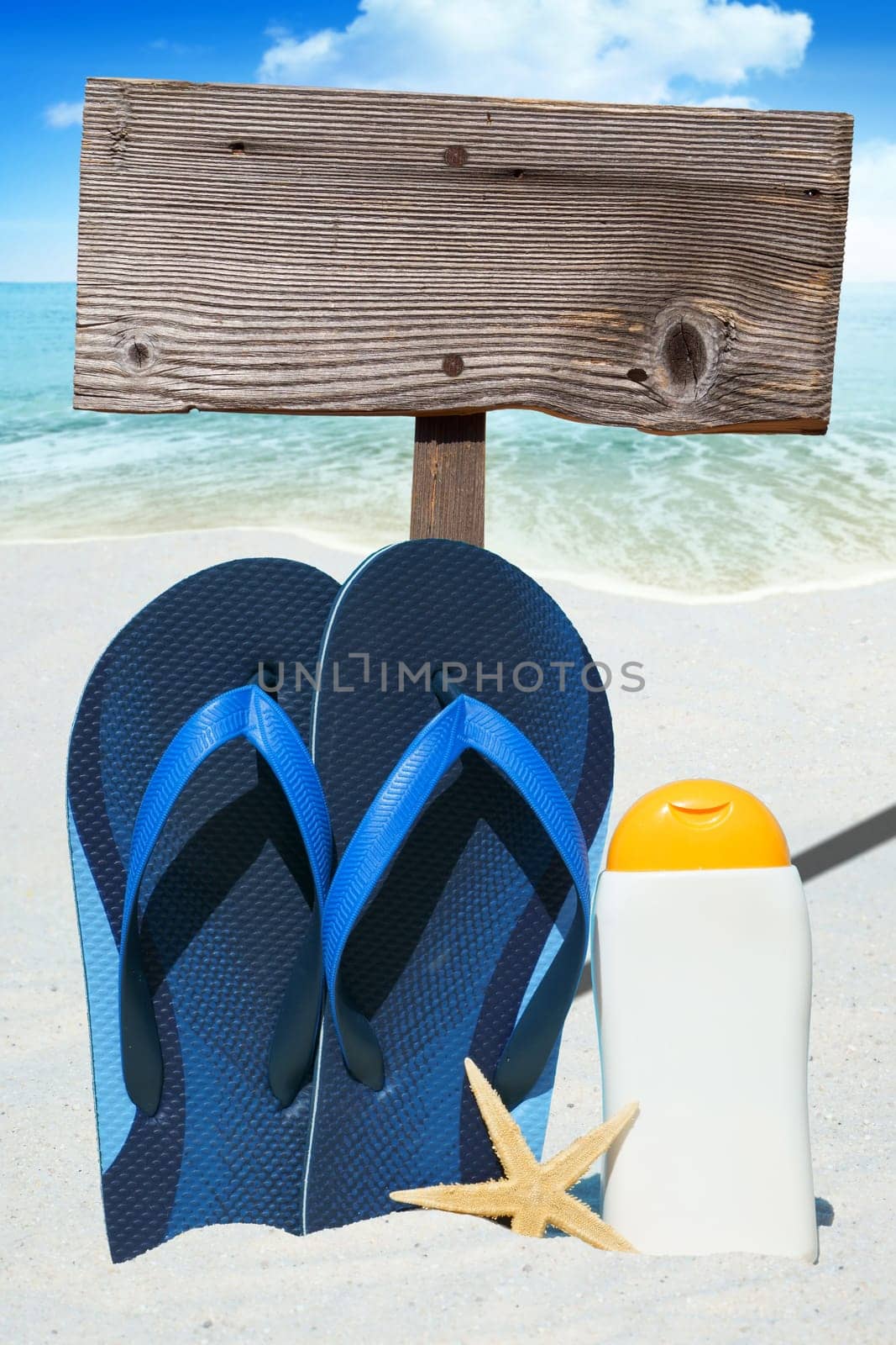 Flip flops,sunmilk and empty wooden sign on the beach