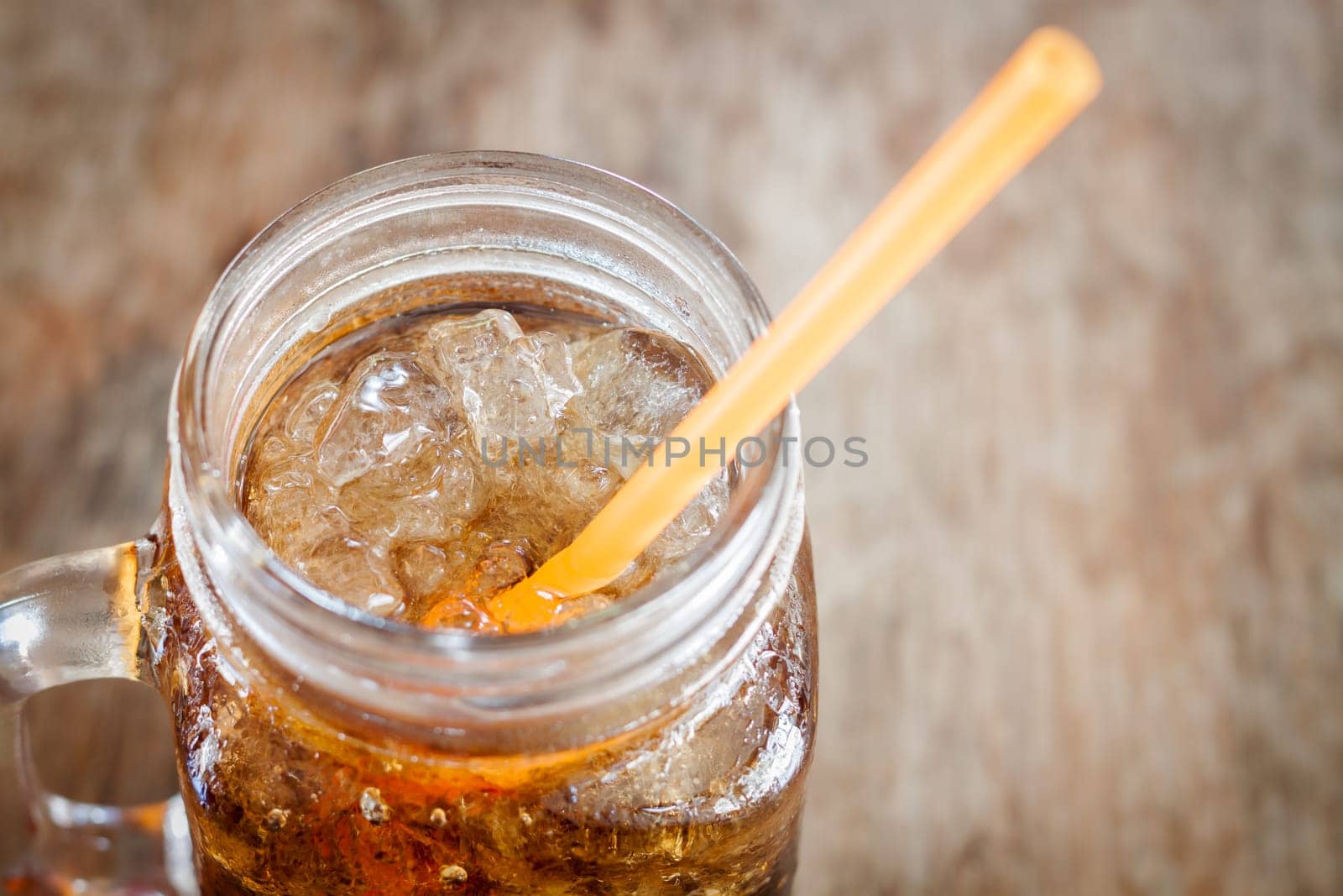 Glass of cola with ice on wooden table, stock photo