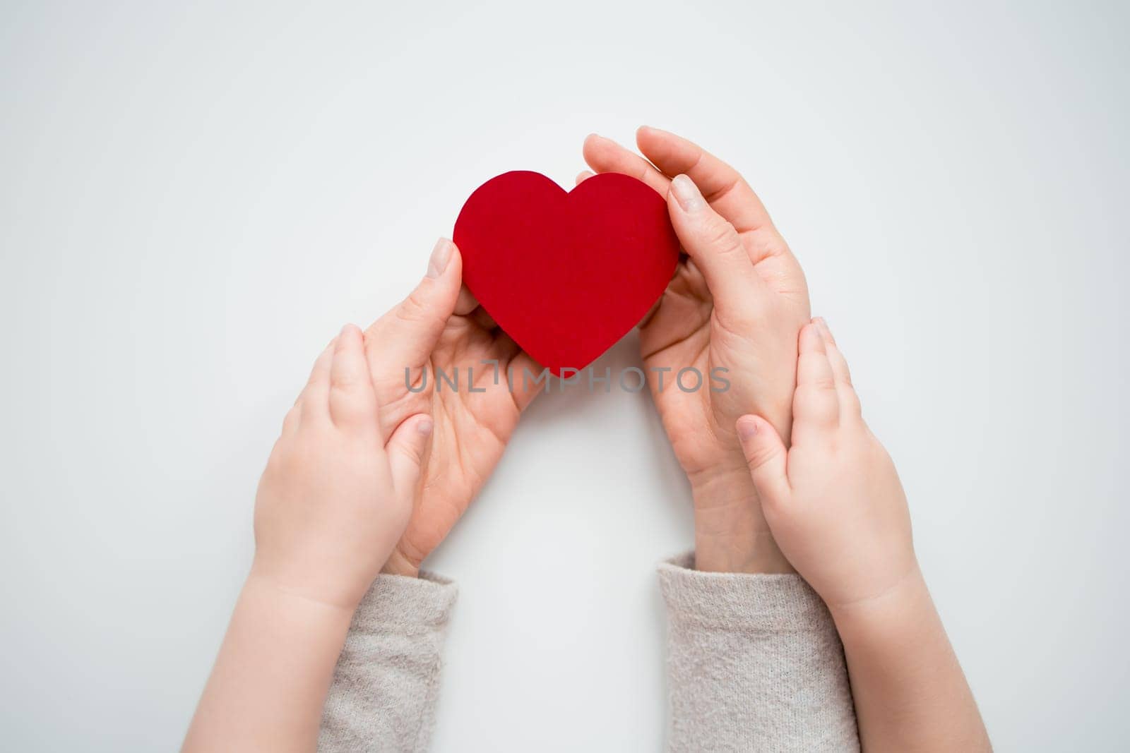 Adult and child holding red heart symbolizing love and care.