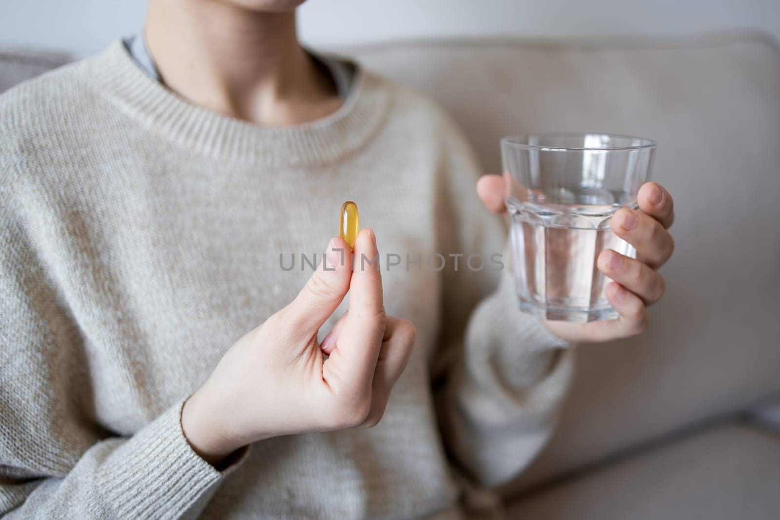Female taking fish oil capsule with water in cozy home setting.
