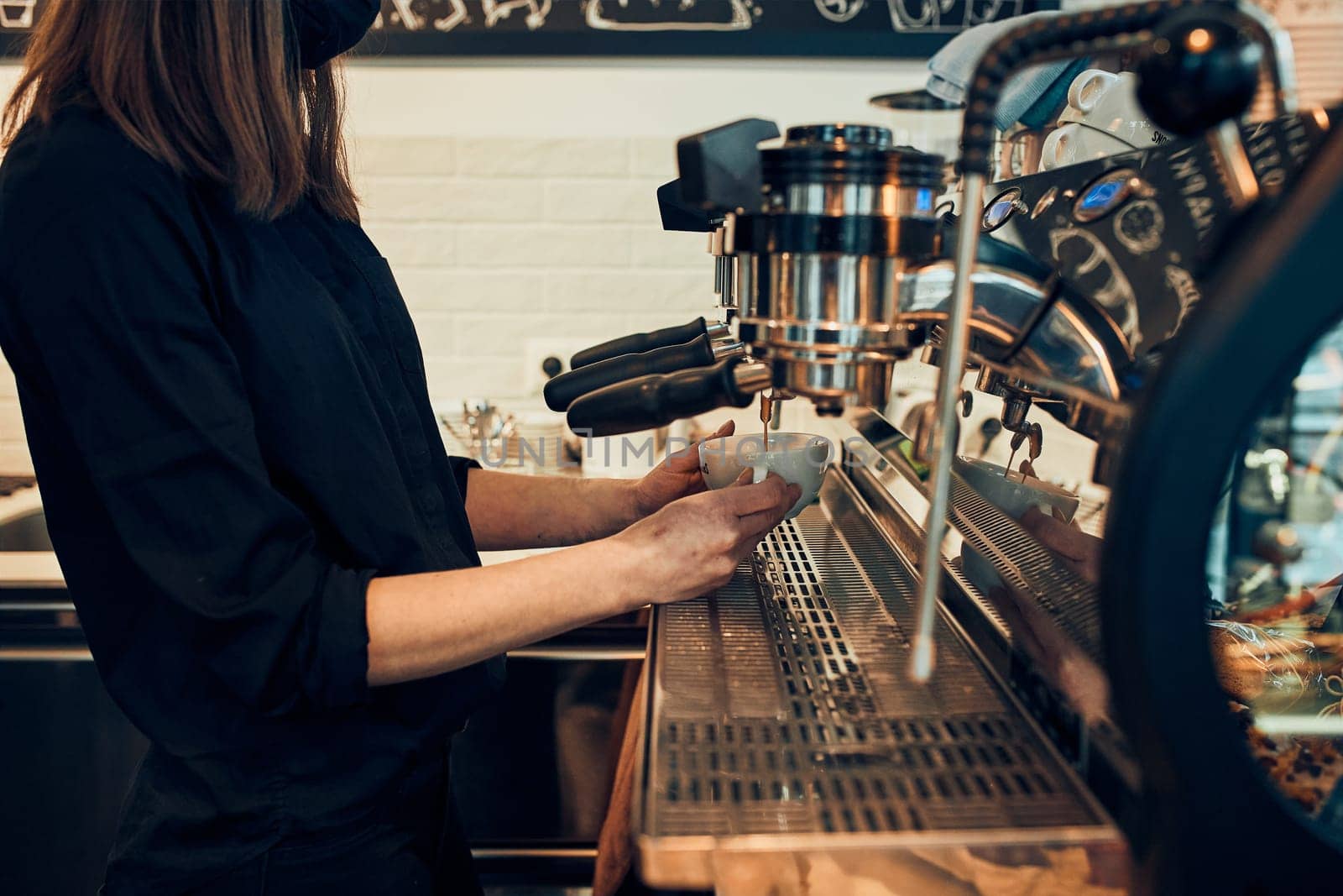 Barista making coffee pouring coffee to a cup making coffee using a coffee maker. Woman bartender making espresso, preparing coffee drink. Young woman working in a coffee shop
